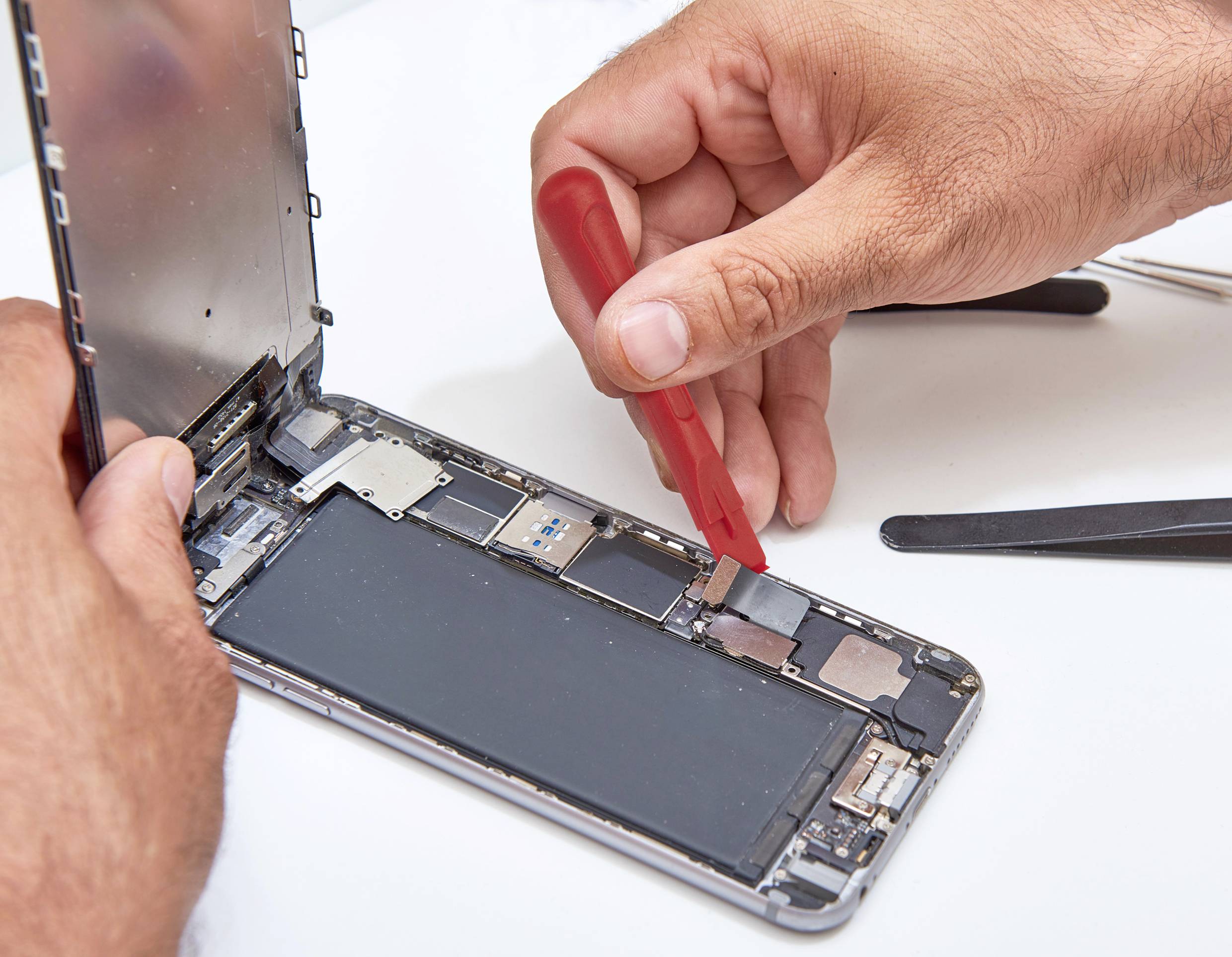 Jedna osoba popravlja pametni telefon tako što podiže zaslon pomoću crvenog alata.