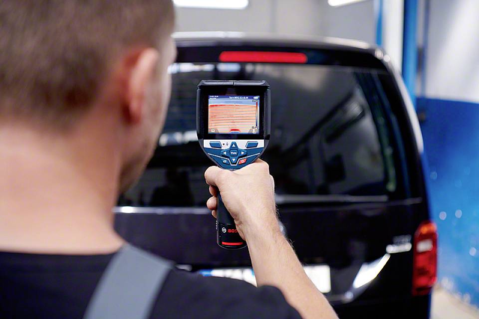 Muškarac koristi infracrveni termometar kako bi izmjerio temperaturu stražnjeg dijela crnog automobila u radionici.