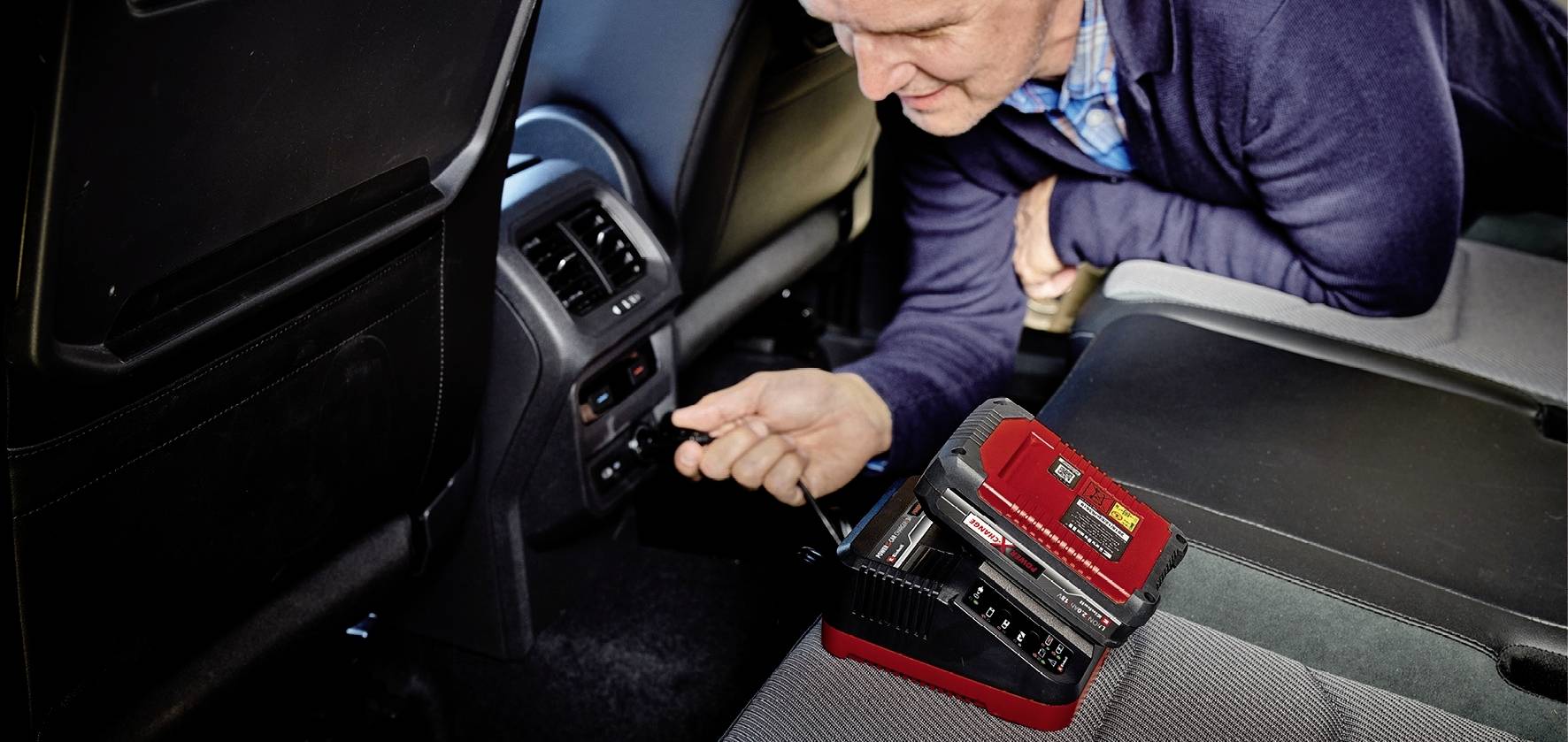 Muškarac instalira elektronički uređaj na stražnjem sjedištu automobila dok radi na priključku u vozilu.