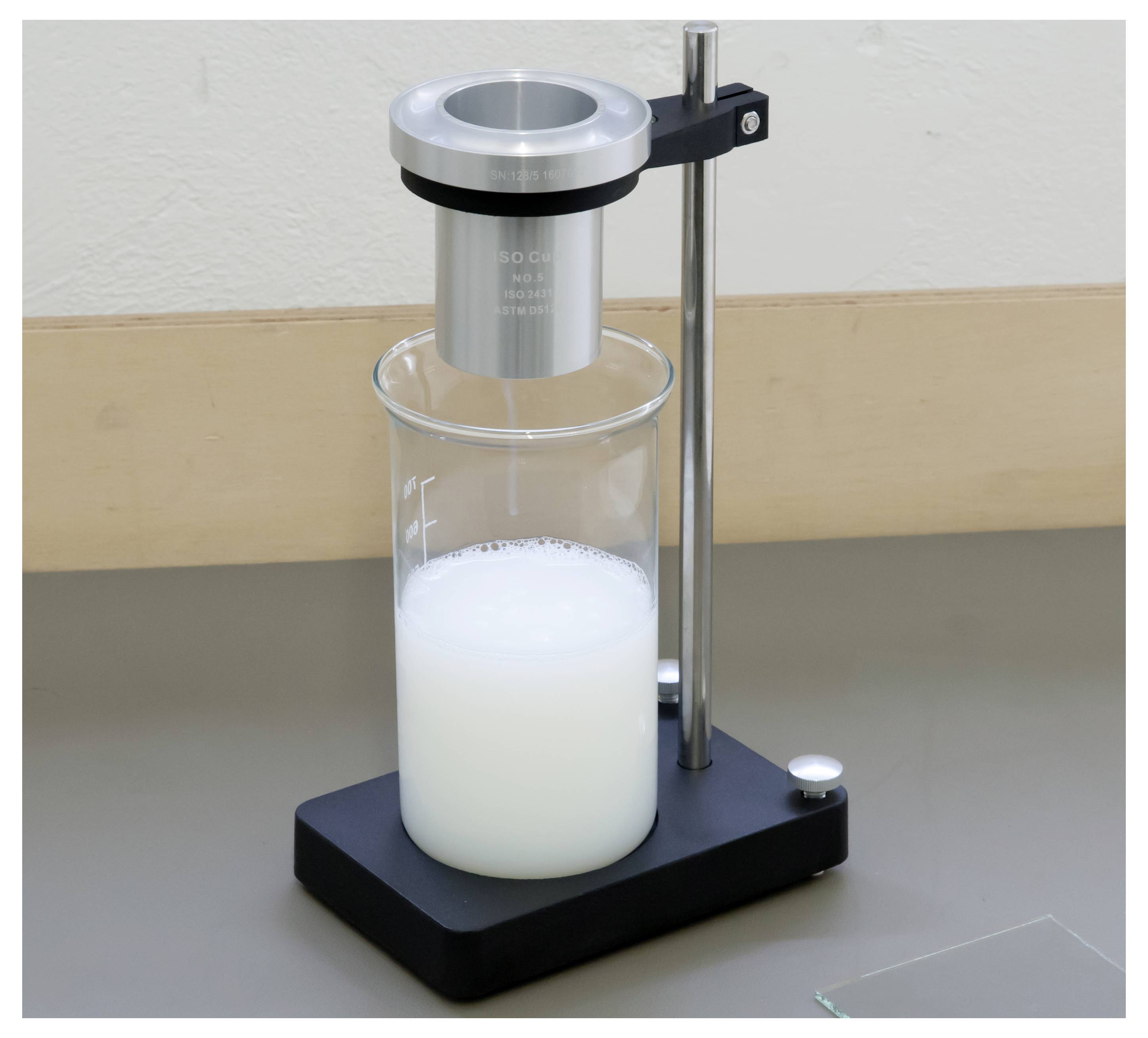 Laboratorijski viskozimetar koji mjeri bijelu tekućinu u čaši na stolnom postolju.