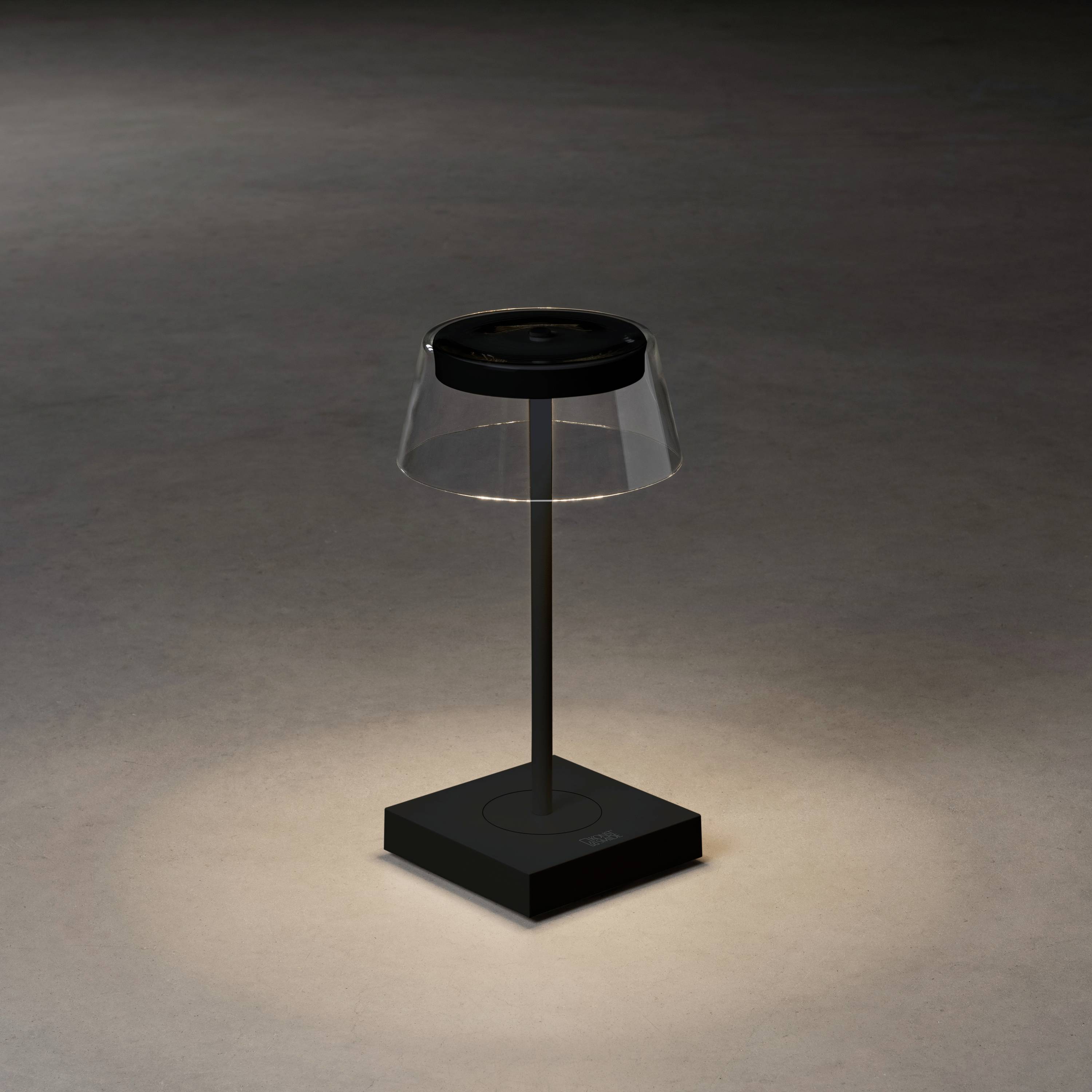 Mala stolna lampa modernog dizajna s prozirnim sjenilom osvjetljava toplo svijetlo na tamnom stolu.