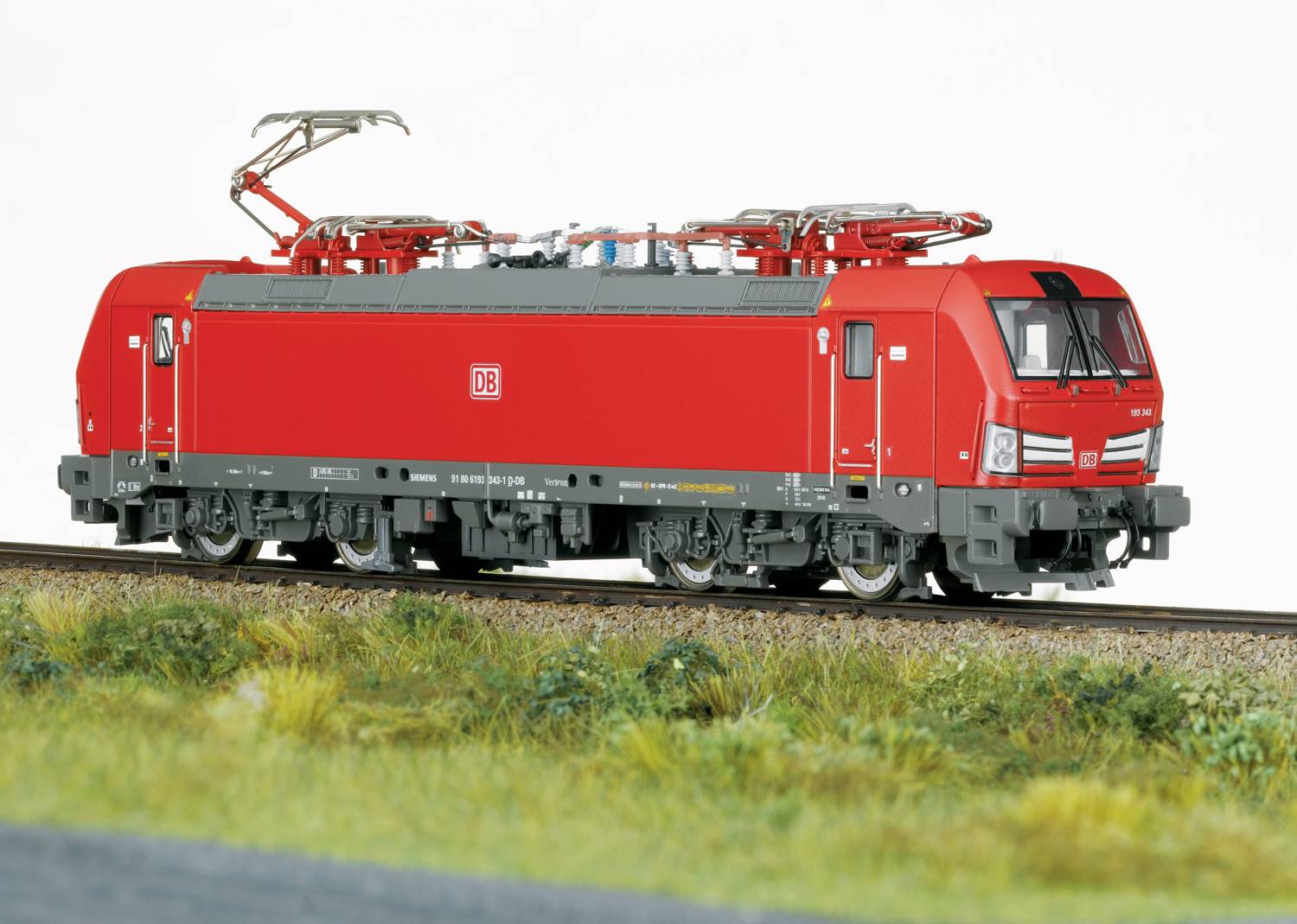Crveni model električne lokomotive Deutsche Bahna na tračnicama, okružen travom.