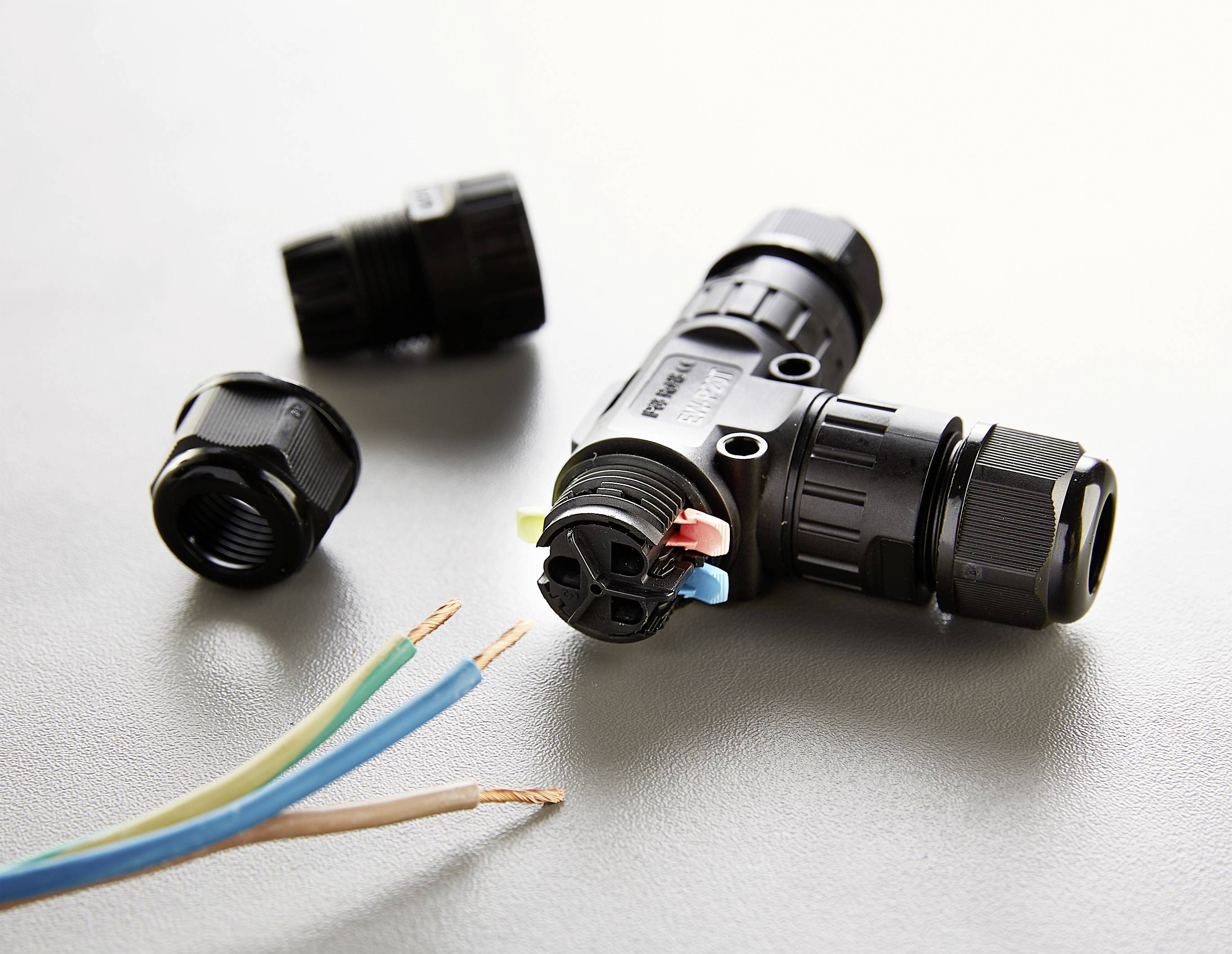 Crni T-razvodnik s priključcima leži na stolu pored tri izložena žica u plavoj, žuto-zelenoj i smeđoj boji.