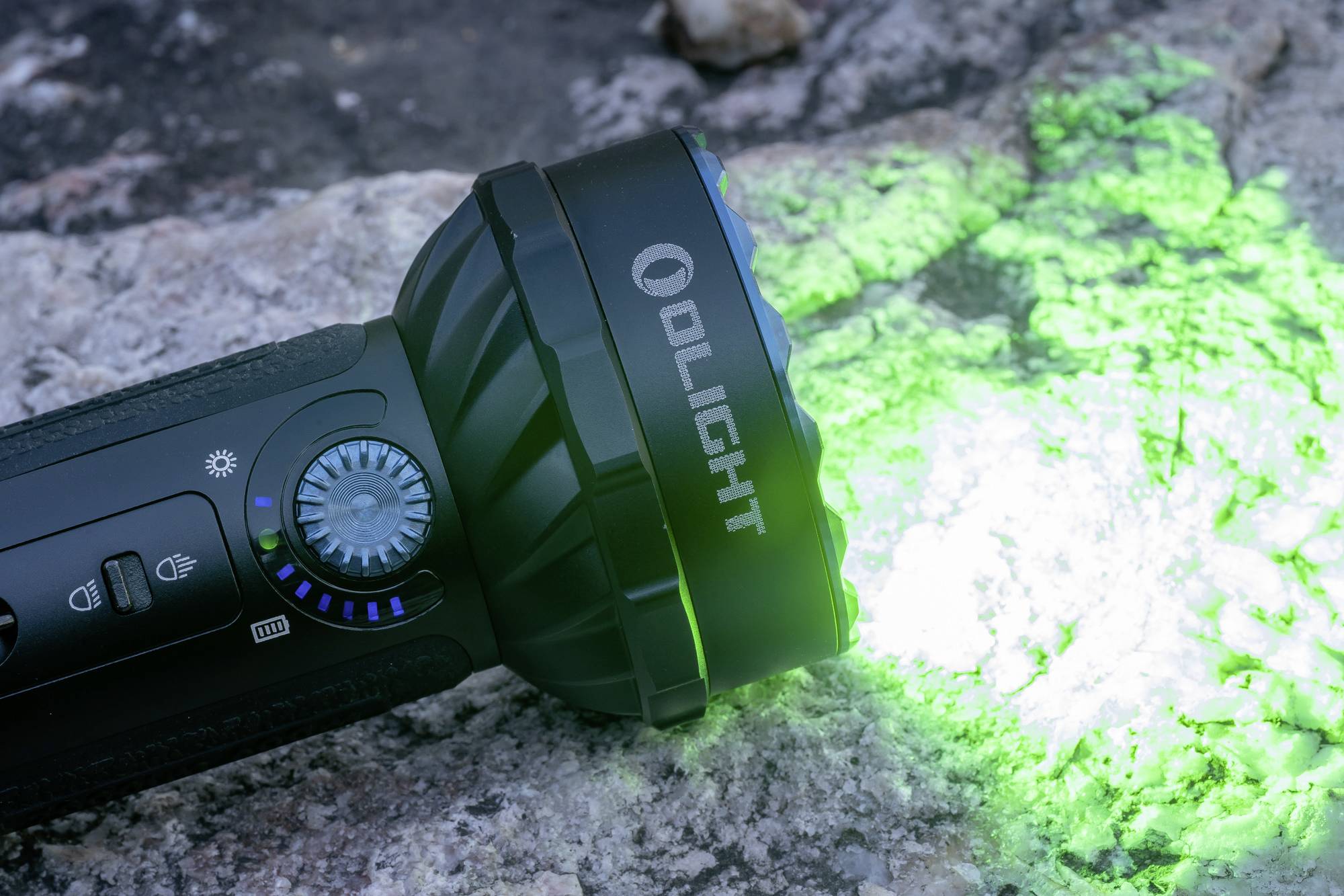 Džepna baterijska lampa sa zelenom svjetlošću osvjetljava kamenu podlogu. Naziv marke 'Olight' vidljiv je sa strane lampe.