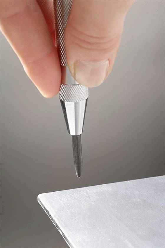 Jedna ruka drži alat sa tankim šiljkom usmjerenim prema rubu metalnog lima.