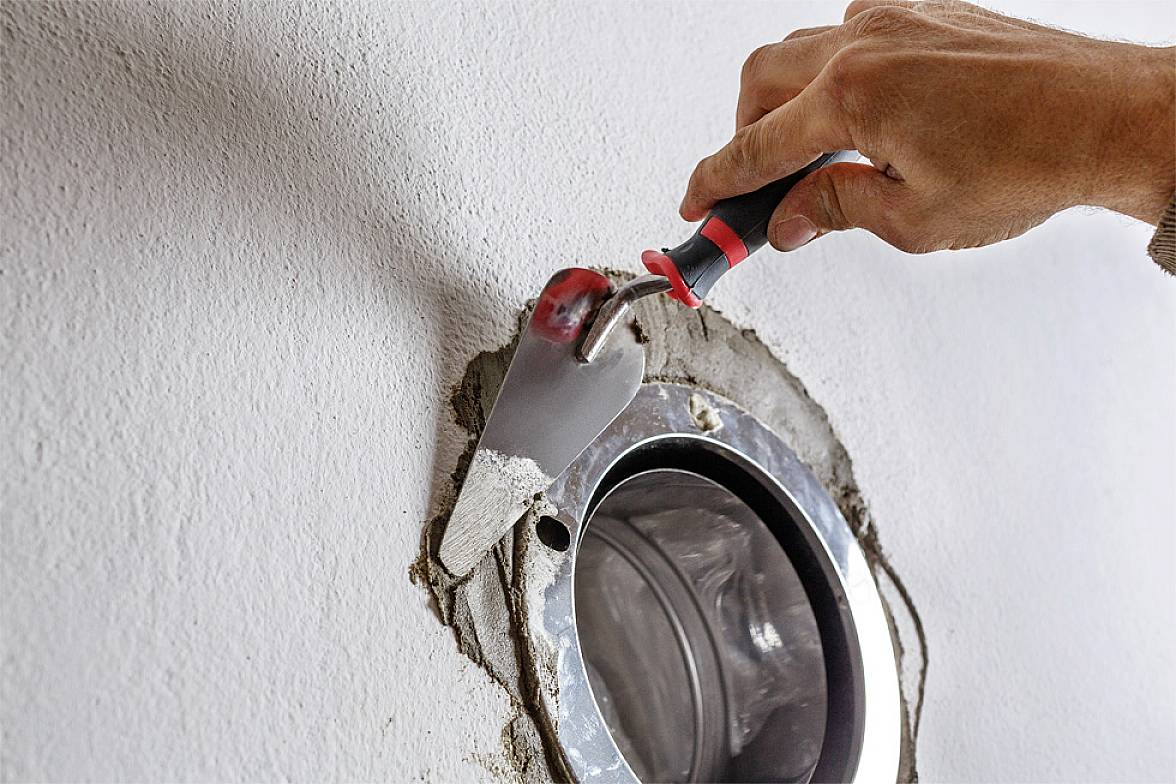 Jedna ruka koristi špahlu kako bi zatvorila otvoreni otvor cijevi u zidu. Obavljaju se radovi renovacije.