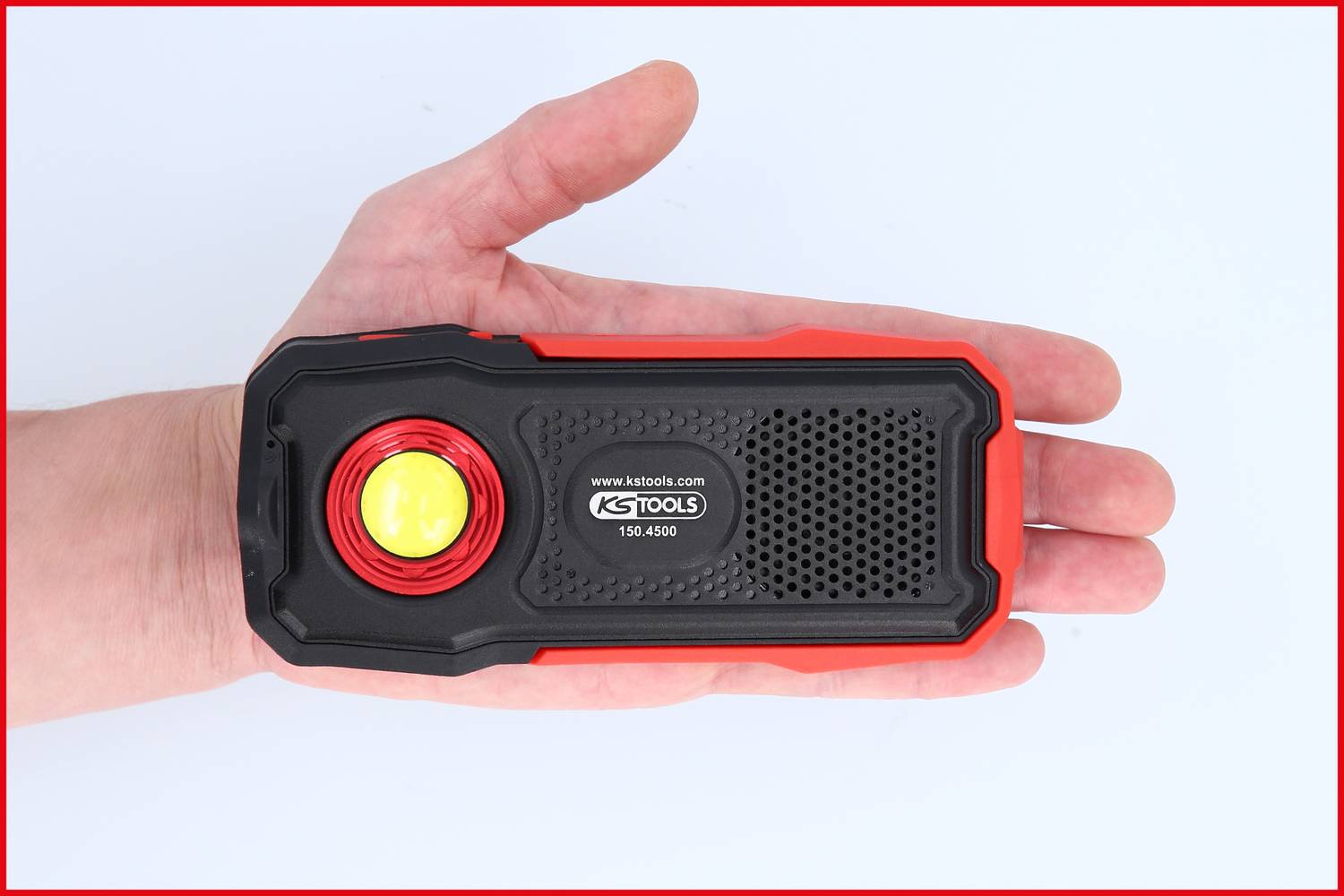Jedna ruka drži crnu, pravokutnu ručnu lampu s crvenim rubom i žutom svjetlošću u sredini, na kojoj piše 'KS TOOLS'.