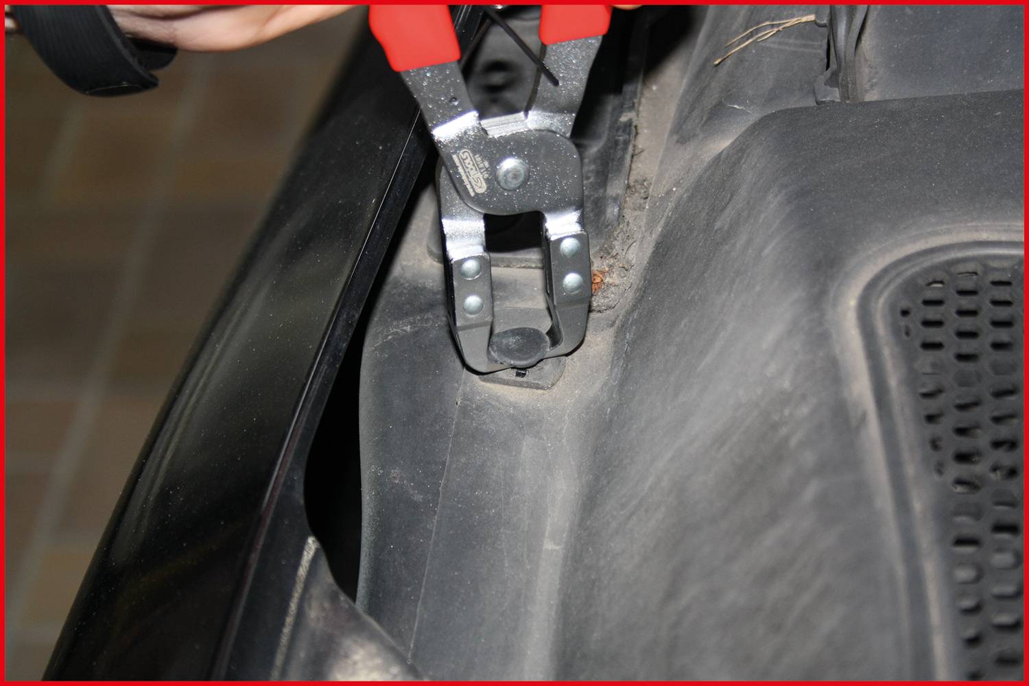 Crvena kliješta uklanjaju čiviju iz crnog plastičnog dijela automobila.