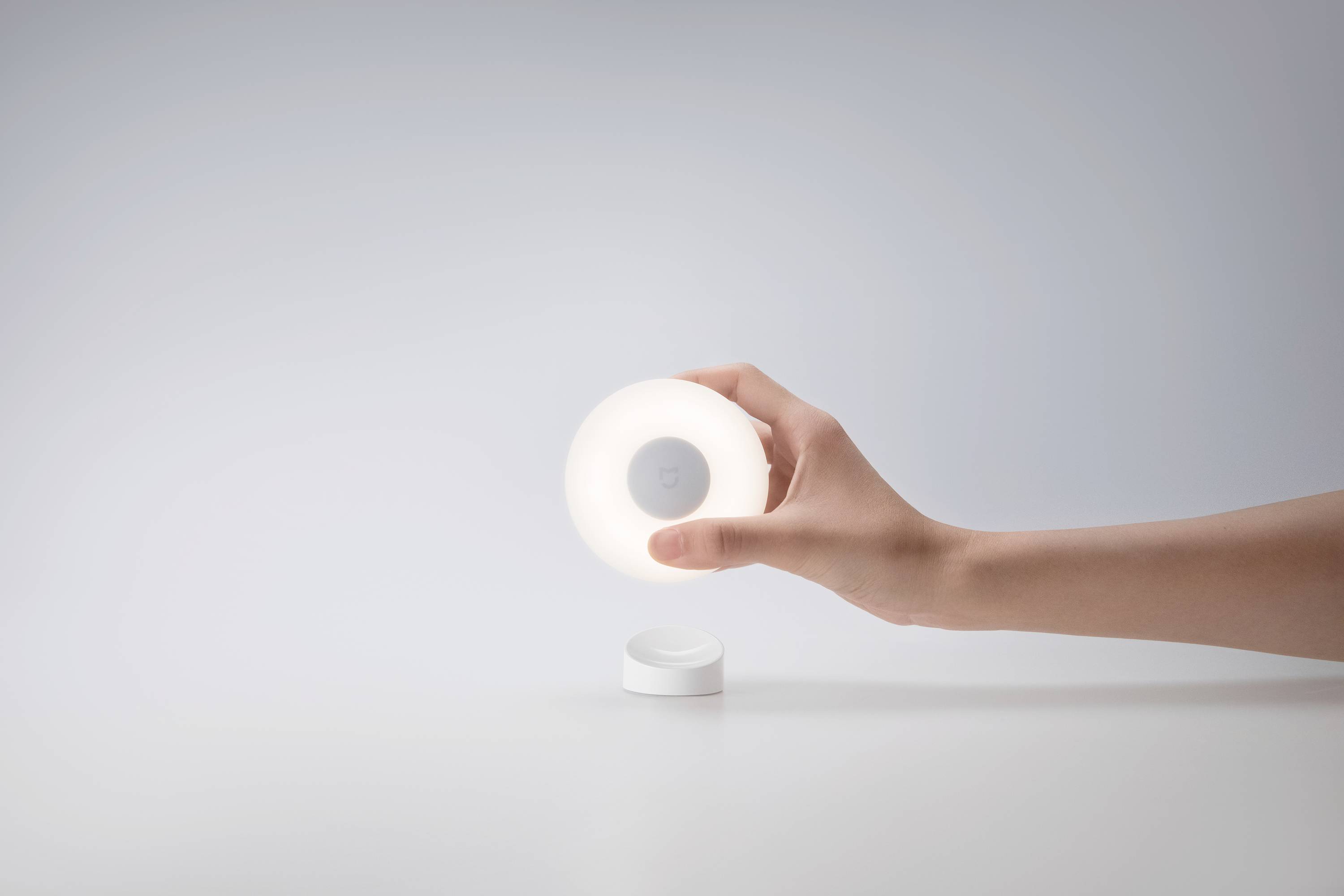 Jedna ruka drži okruglu, sjajnu noćnu lampu iznad bijele pozadine.