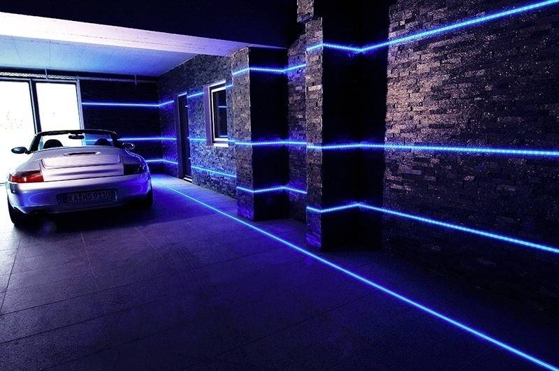 Srebrni automobil parkiran je u garaži s tamnim zidovima koji su naglašeni plavim LED-trakom.