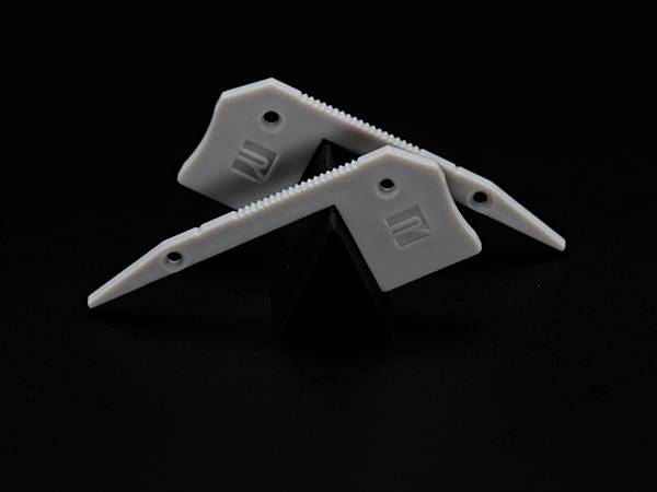 Dva bijela plastična objekta nazubljivih rubova i s rupicama leže na crnoj pozadini. Čine simetrični uzorak.