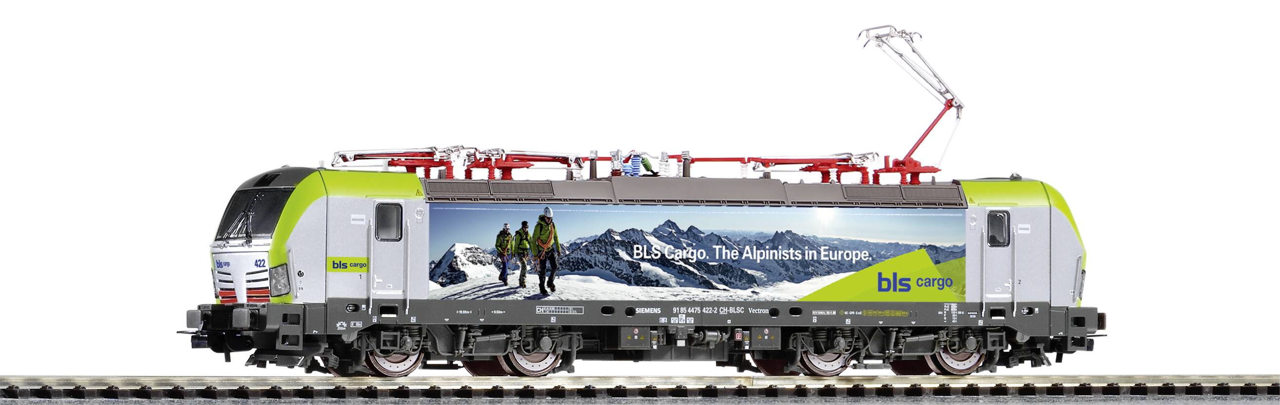 Modelna željeznica s reklamnom slikom Alpi i tekstom 'BLS Cargo: Alpe - nisu onakve kakve se čine u Europi'. U pozadini planine.