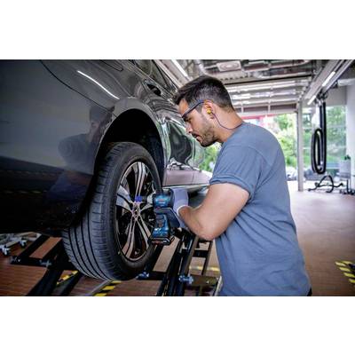 Mehaničar popravlja gumu automobila u radionici. Koristi električni alat i nosi zaštitu za uši.