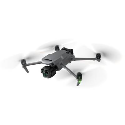 Siva dron u letu s četiri rotora i kamerom na prednjoj strani, propeleri nejasni zbog pokreta, bijela pozadina.