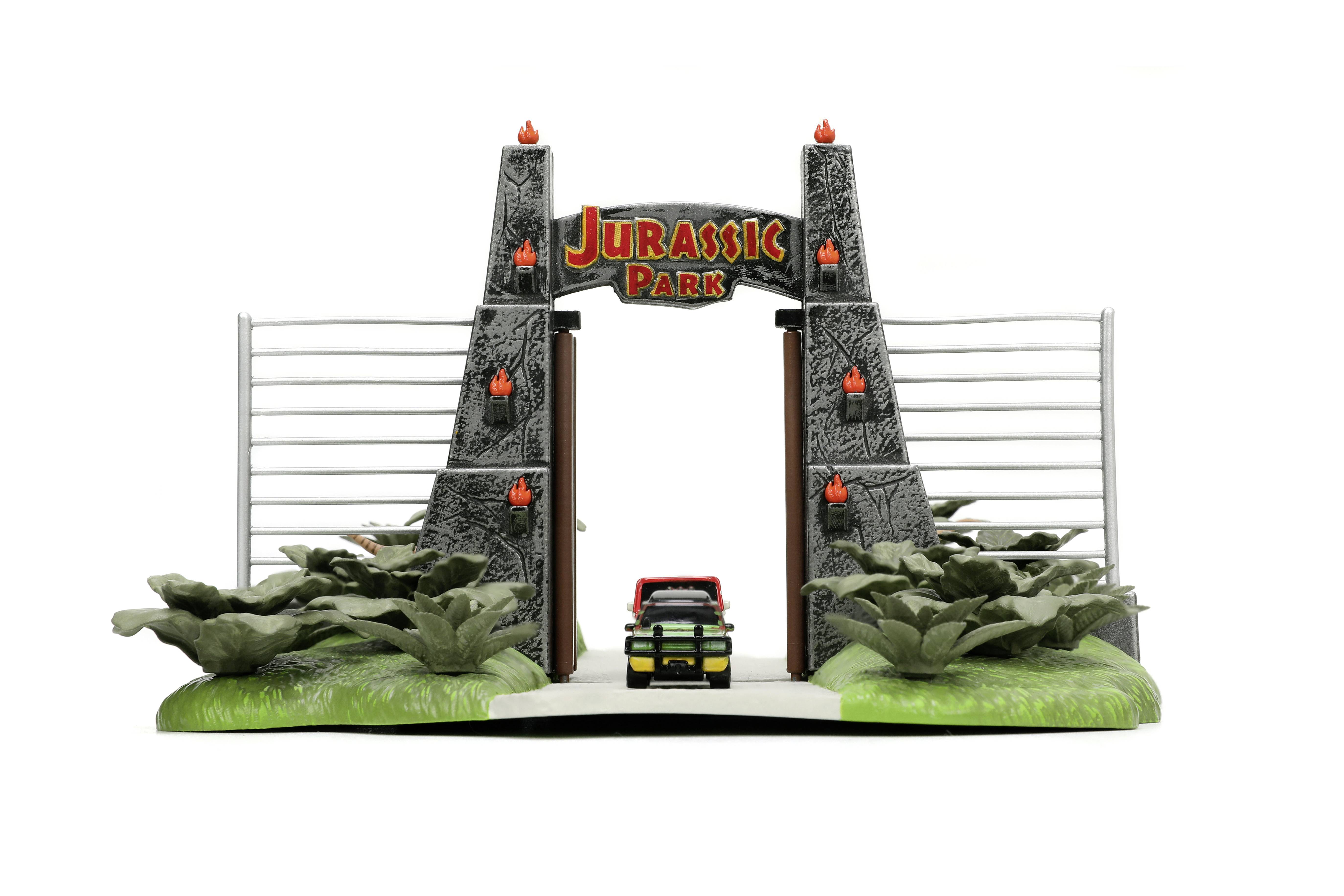 Model ulazne kapije sa znakom 'Jurassic Park', crvenim Jeepom i umjetnim biljem, sličan sceni iz filma.