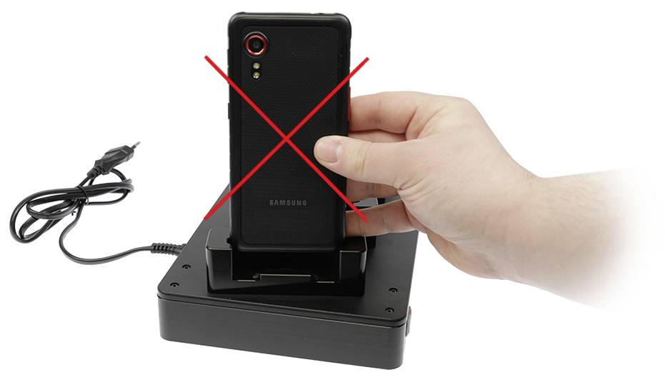 Jedna ruka drži pametni telefon iznad punjača koji stoji na stolu. Crveni X pokazuje da to nije dopušteno.