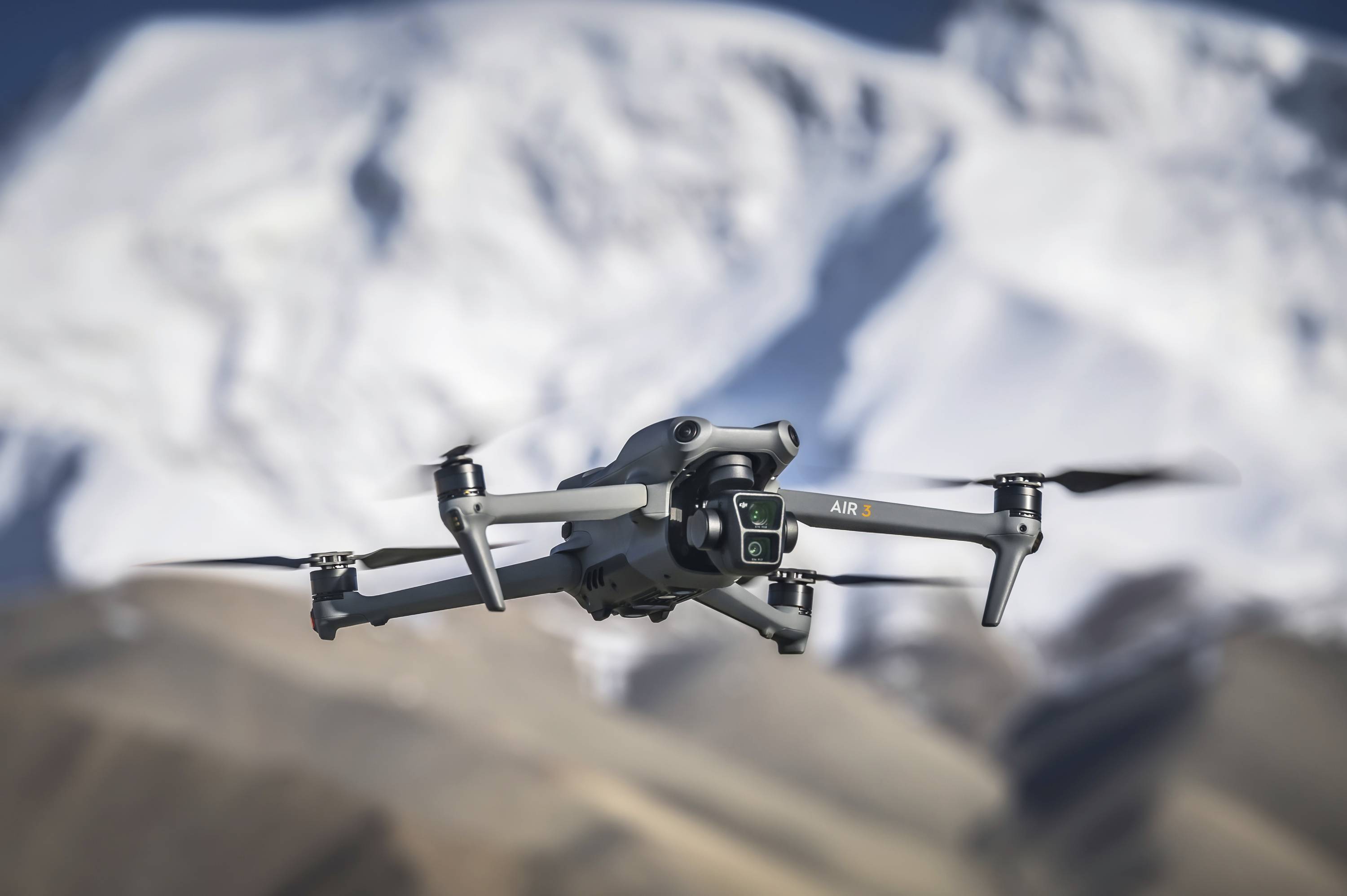 Dron leti ispred snijegom pokrivene planinske krajoline. Ima četiri propelera i kameru na prednjoj strani.