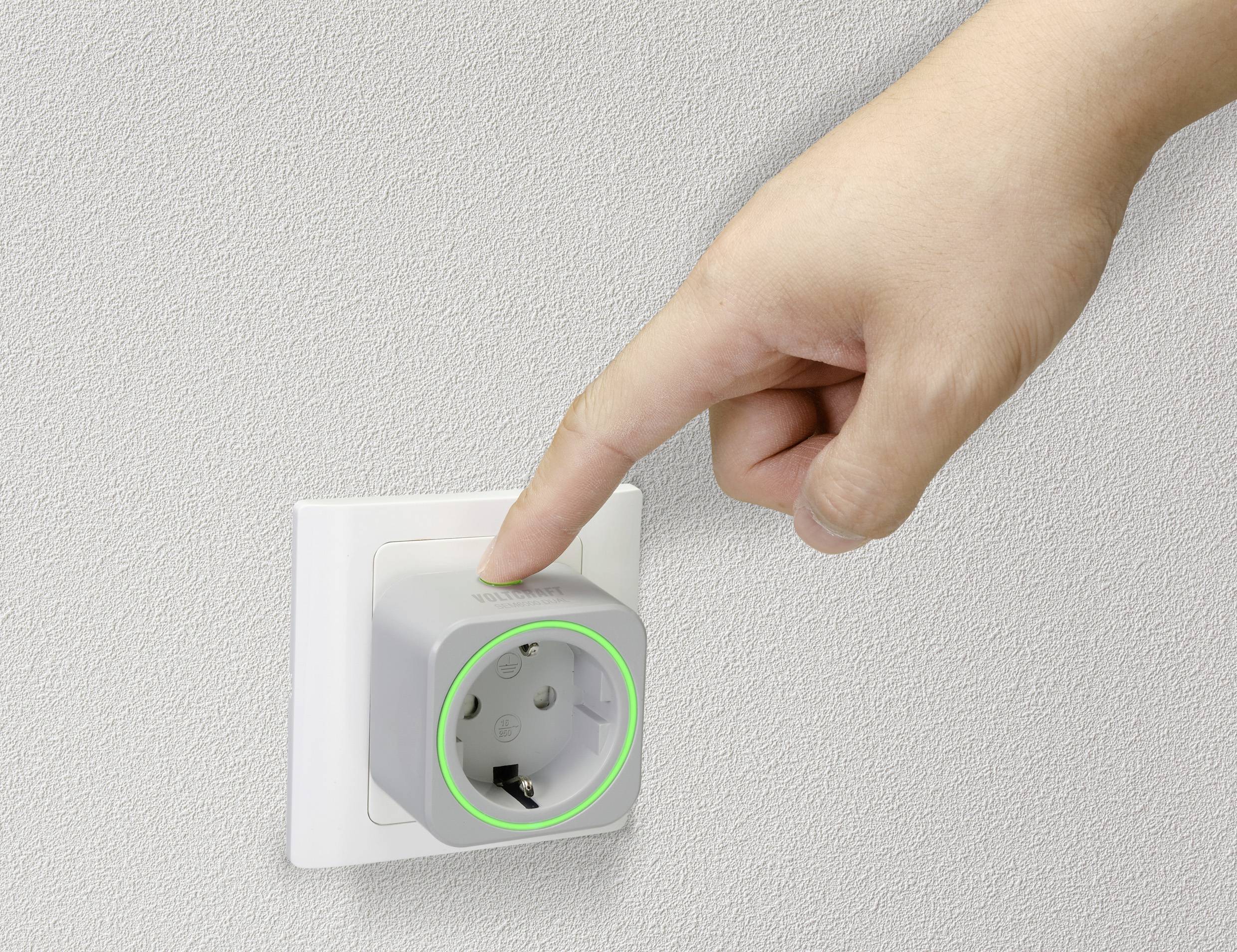 Prst pokazuje na pametnu utičnicu s svjetlećim zelenim prstenom ugrađenu u zidnu utičnicu.