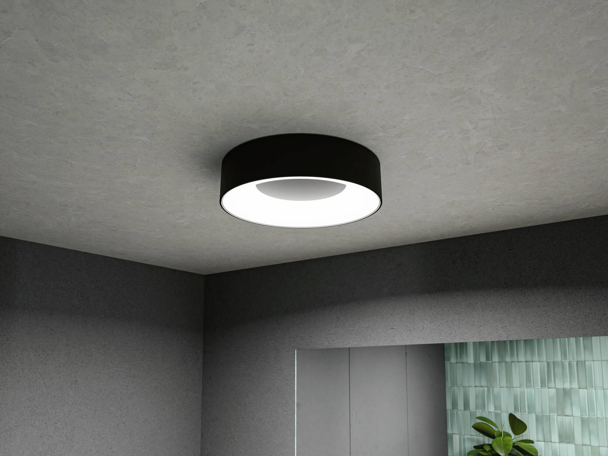 Okrugla, moderna stropna lampa osvjetljava prostoriju. Zidovi su sivi, biljka je vidljiva u kutu.