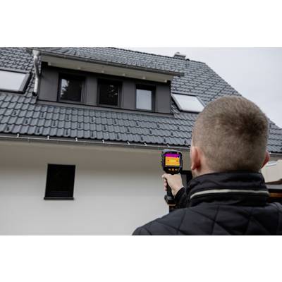 Jedna osoba usmjerava termičku kameru prema krovu kuće. Kamera prikazuje termalni snimak za provjeru izolacije.