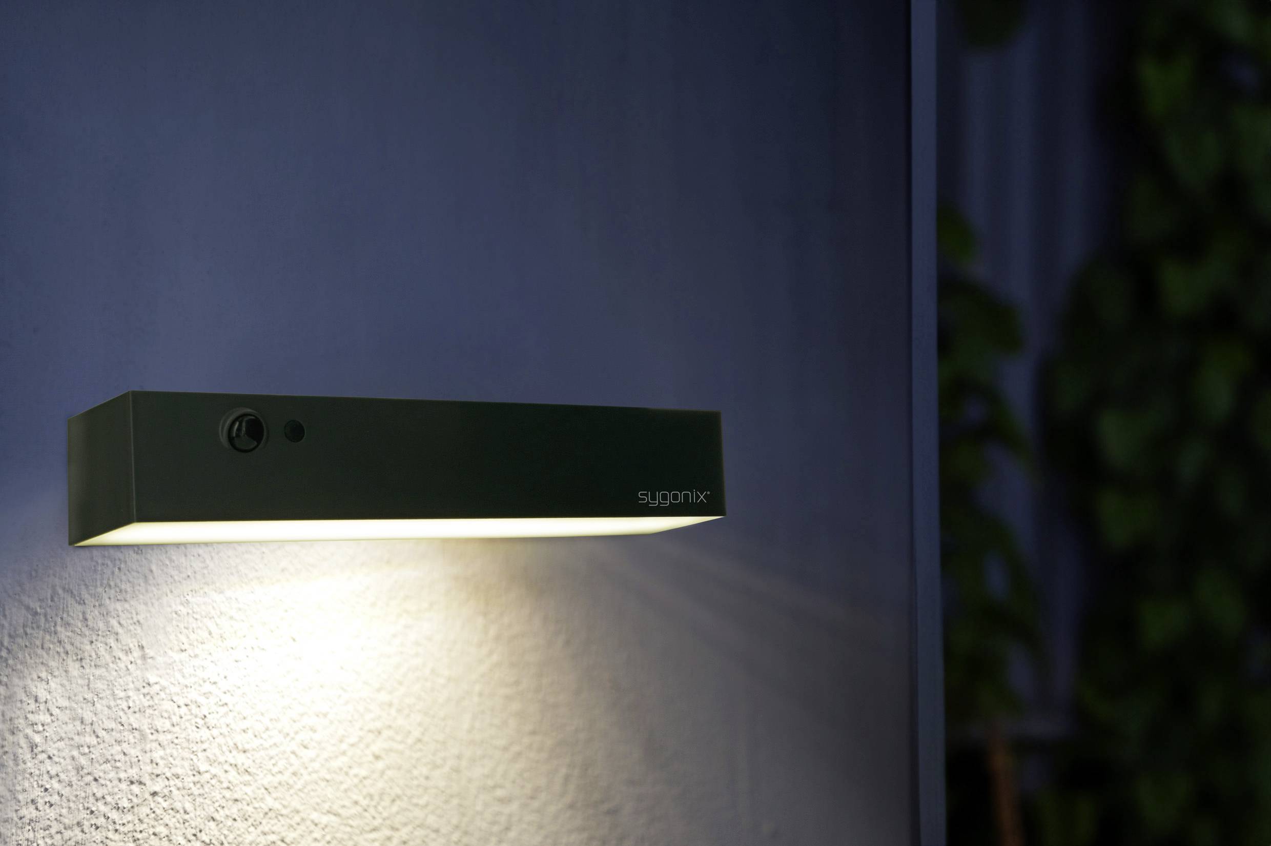 Pravokutna, moderna lampa obasjavala je zid toplim svjetlom.