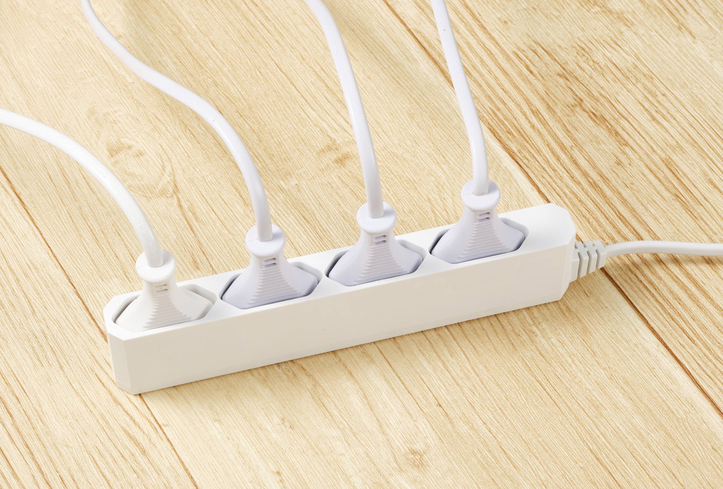 Bijela razvodna letva s četiri uključena električna kabela leži na drvenom stolu.