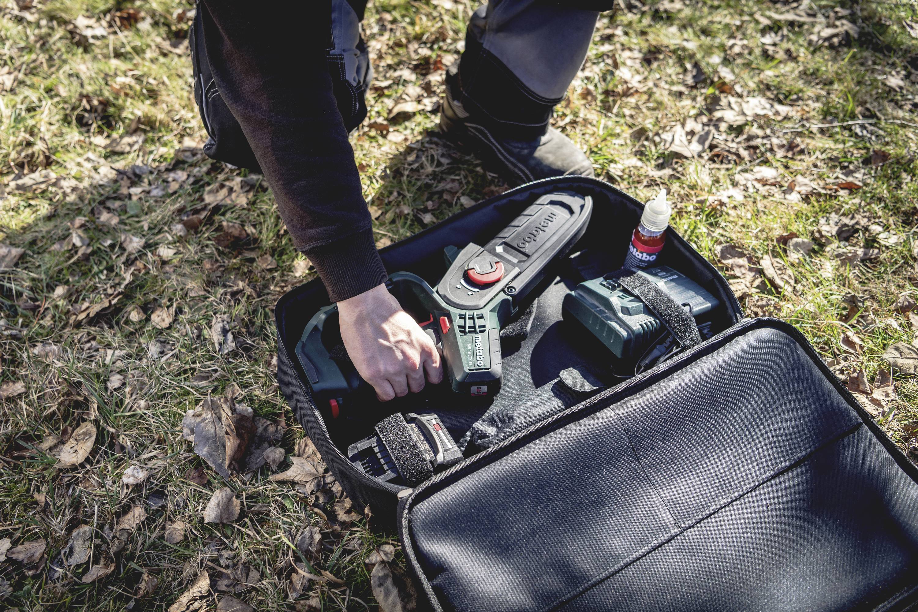 Jedna osoba na otvorenom otvara crni kovčeg za alat koji sadrži zeleni električni alat i pribor.