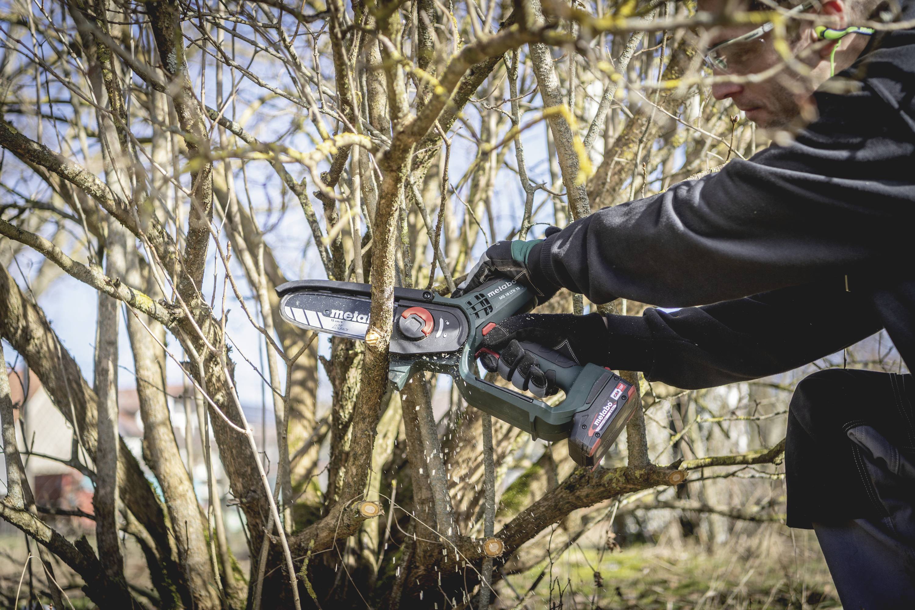 Osoba reže grane motornom pilom. Fokus je na pile i tehnici rezanja.