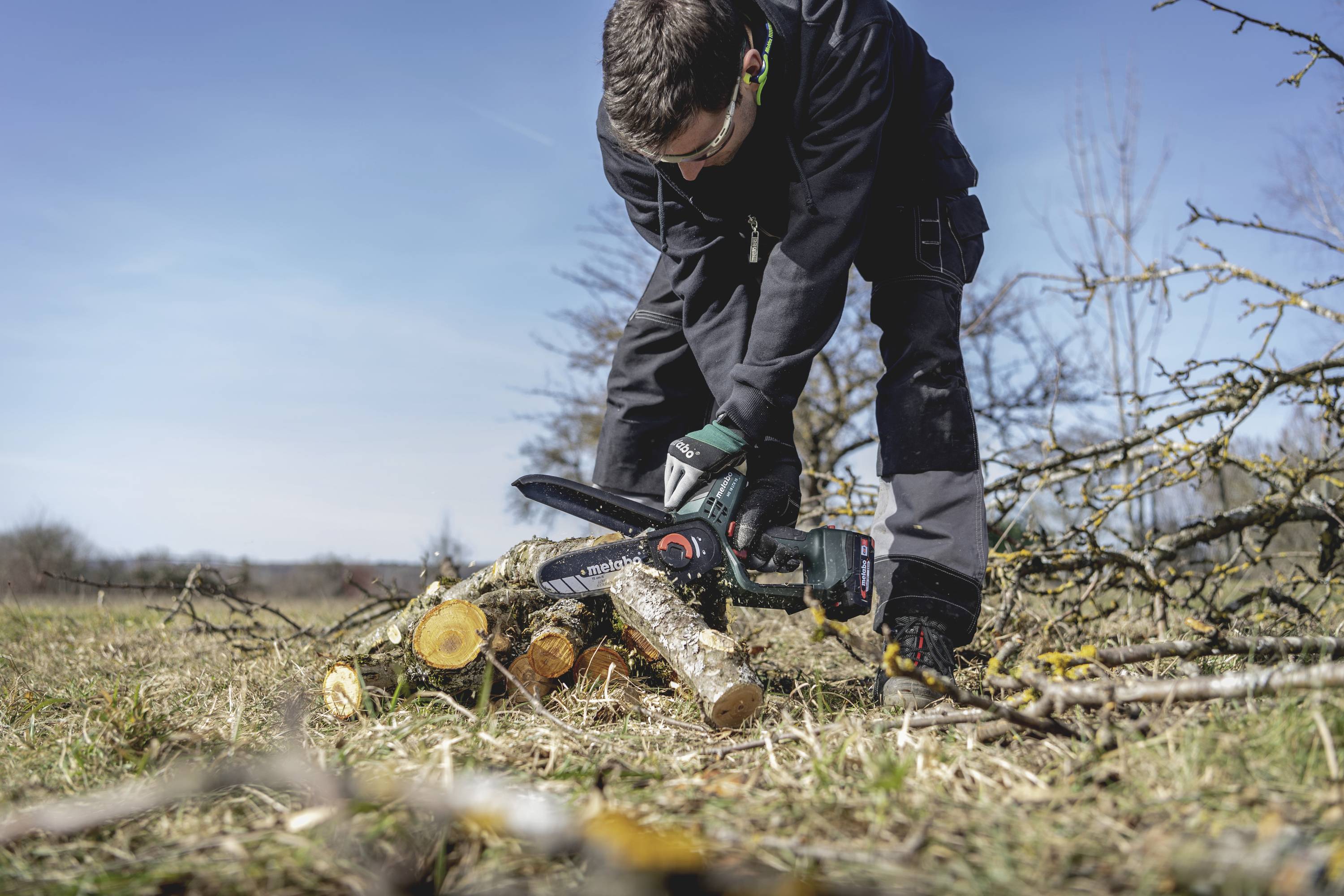 Osobareže drva motornom pilom na livadi vani.