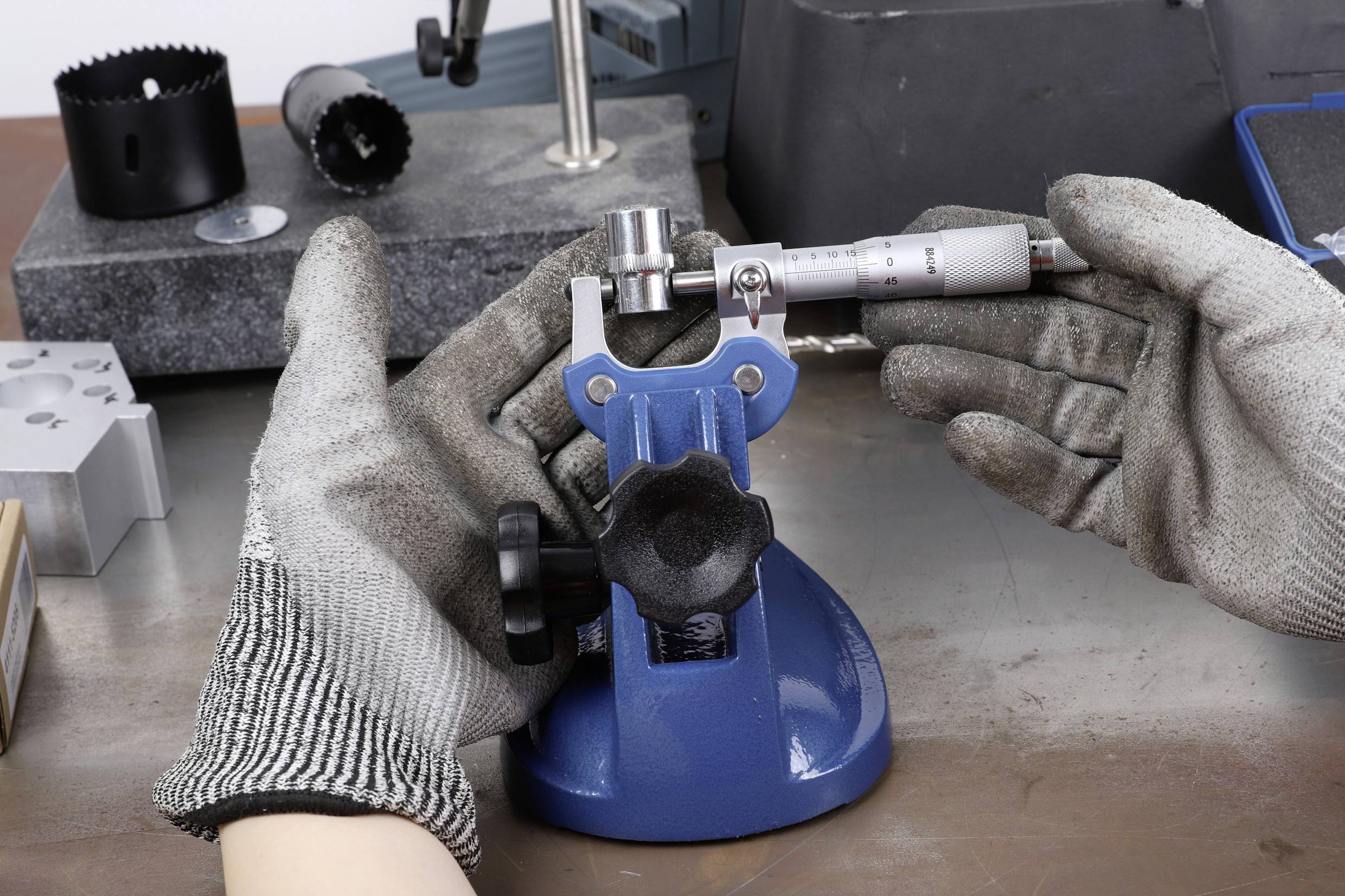 Jedna osoba koristi mikrometar za mjerenje malog cilindričnog objekta postavljenog na plavom stalku.