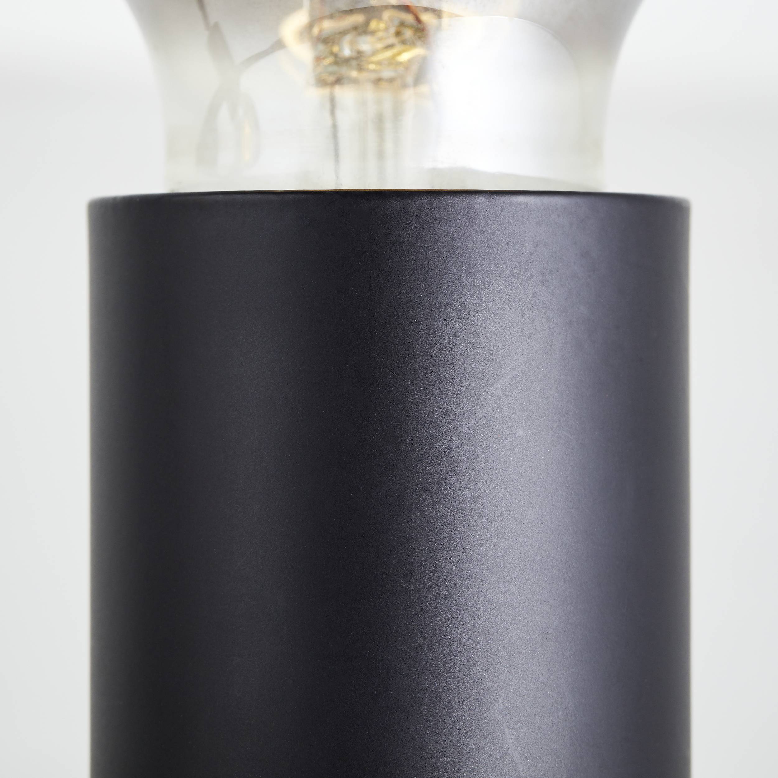 Bliski kadar dijela crne cilindričke lampe. Gore u staklenom poklopcu vidljiva je užarena žica.