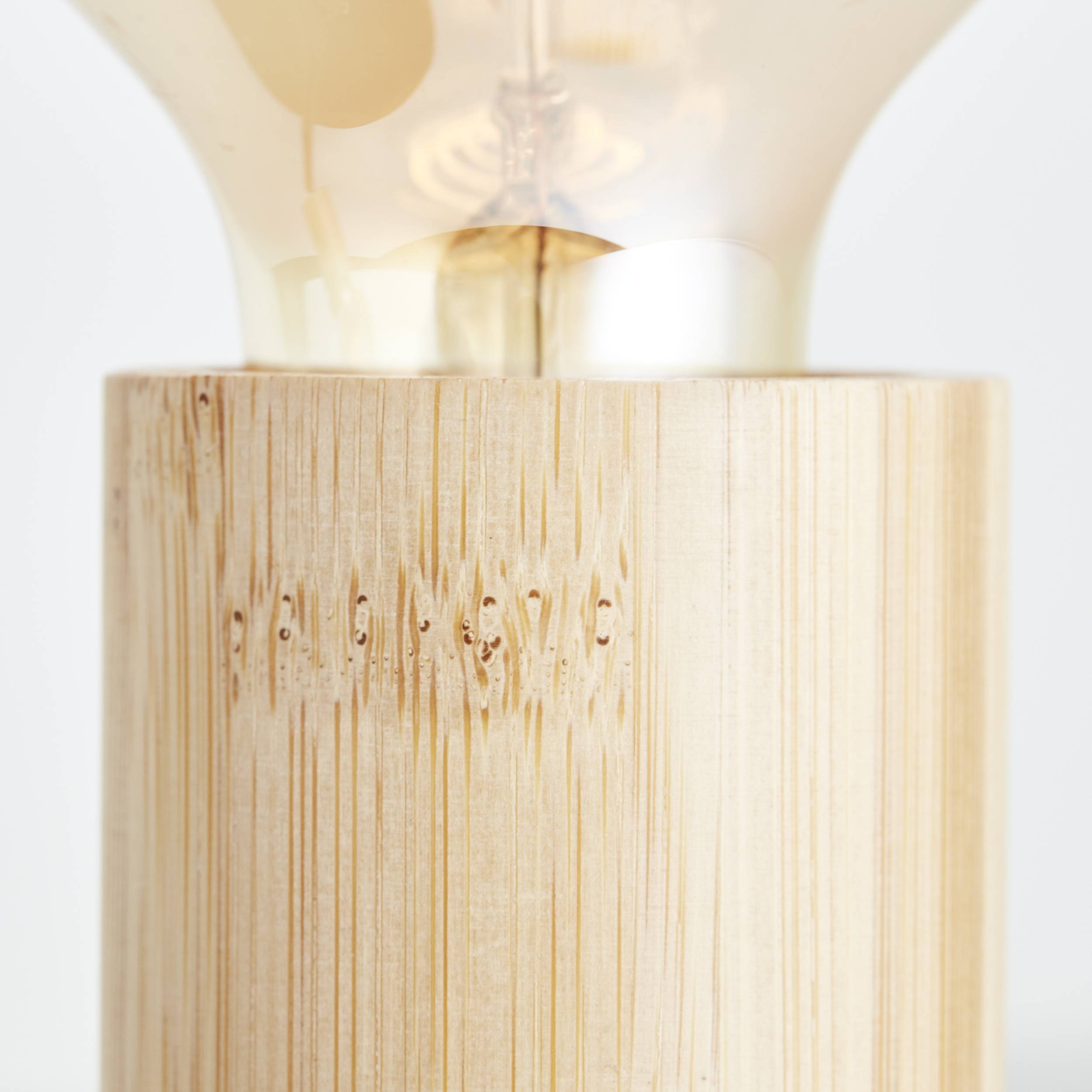 Bliski kadar drvene lampe s vidljivim dijelom žarulje. Podnožje lampe izrađeno je od natural­nog, svijetlog drveta.