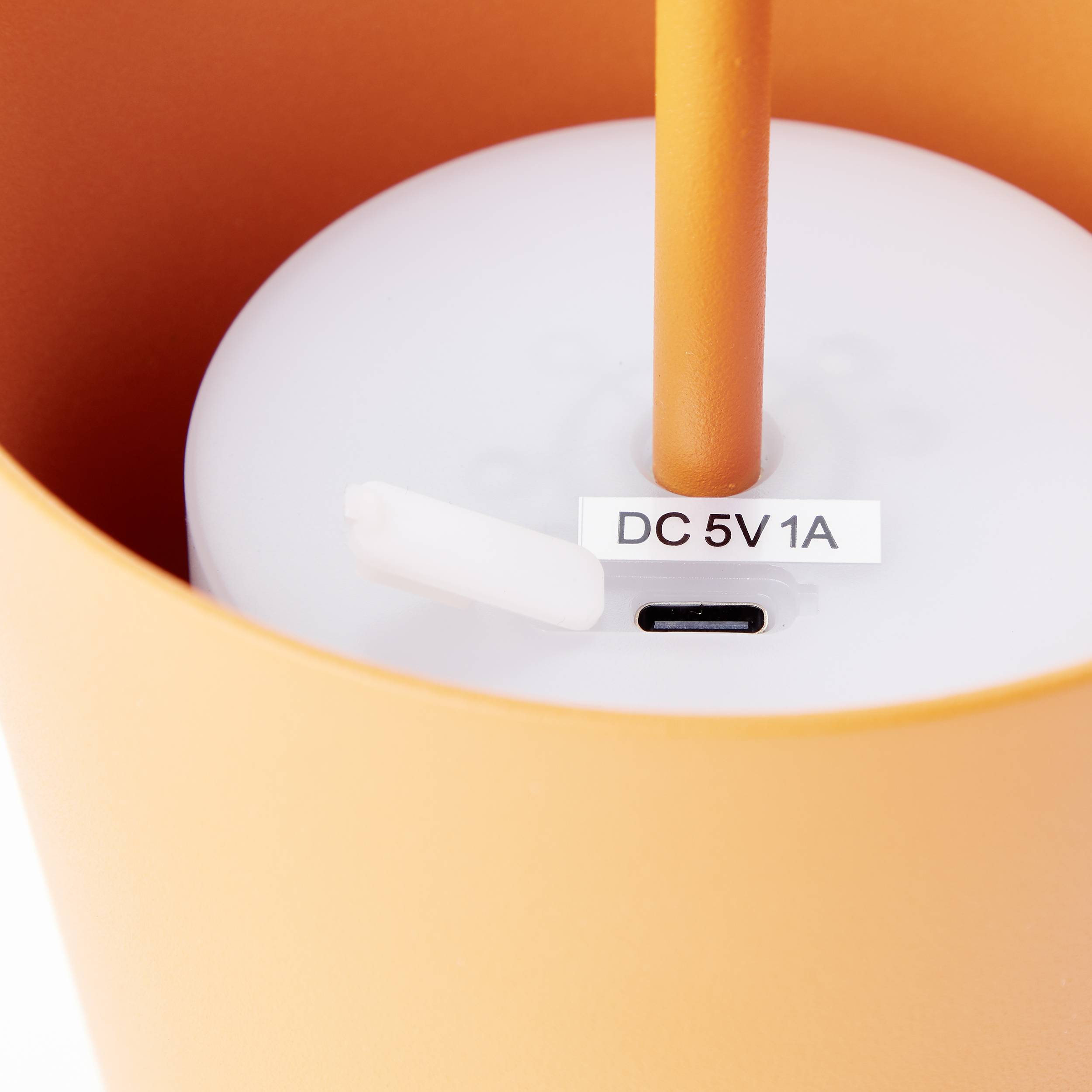 Priključak "DC 5V 1A" na donjoj strani narančastog elektroničkog uređaja.