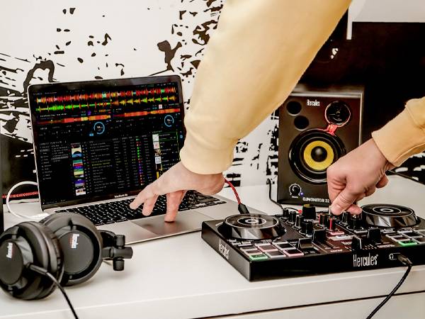 Jedna osoba koristi DJ-kontroler s prijenosnim računalom i zvučnikom. Na prijenosnom računalu je otvorena DJ-softver s više glazbenih zapisa.