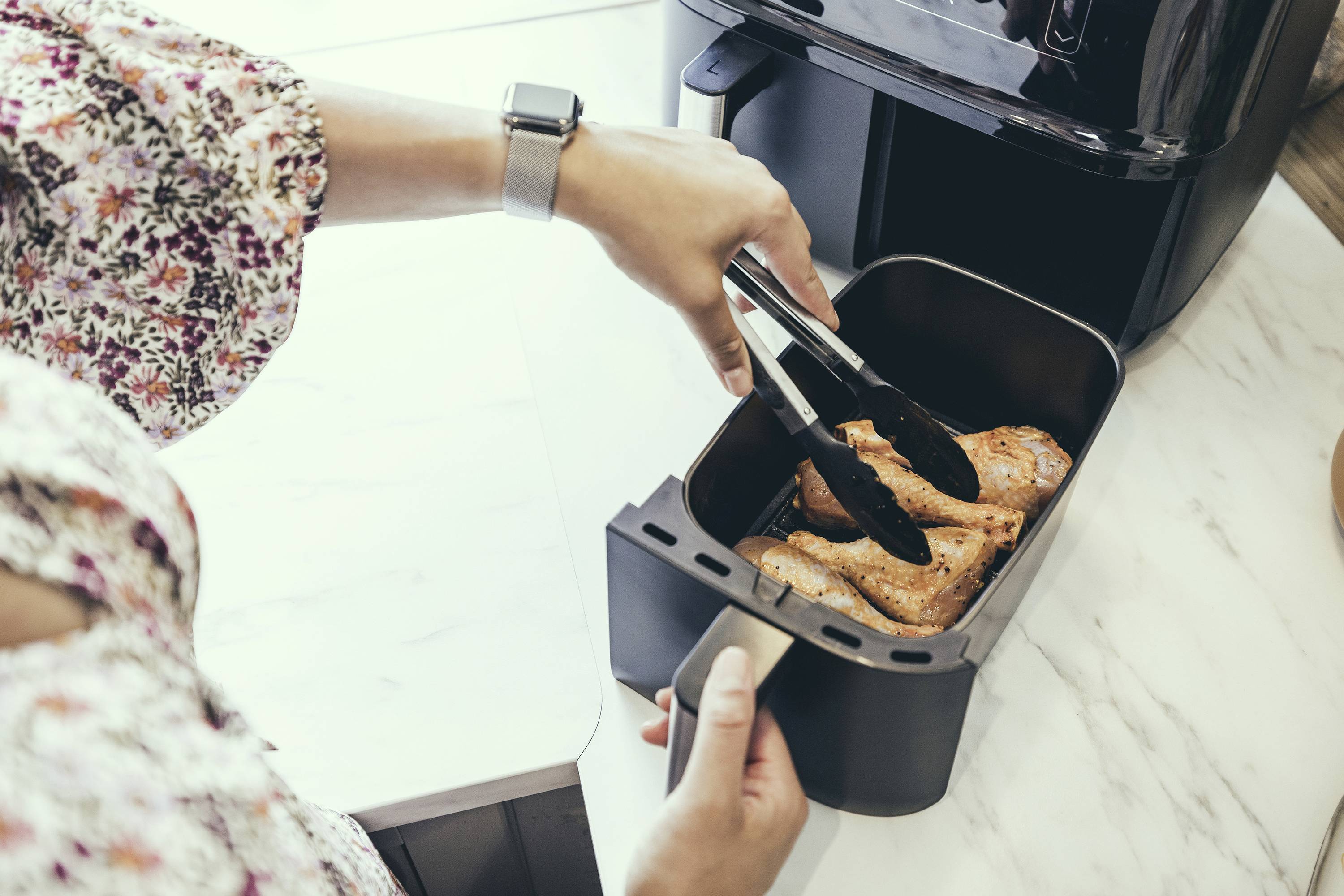 Osoba kliještima stavlja pečene pilanske batke u posudu za air fryer na kuhinjskoj radnoj ploči.