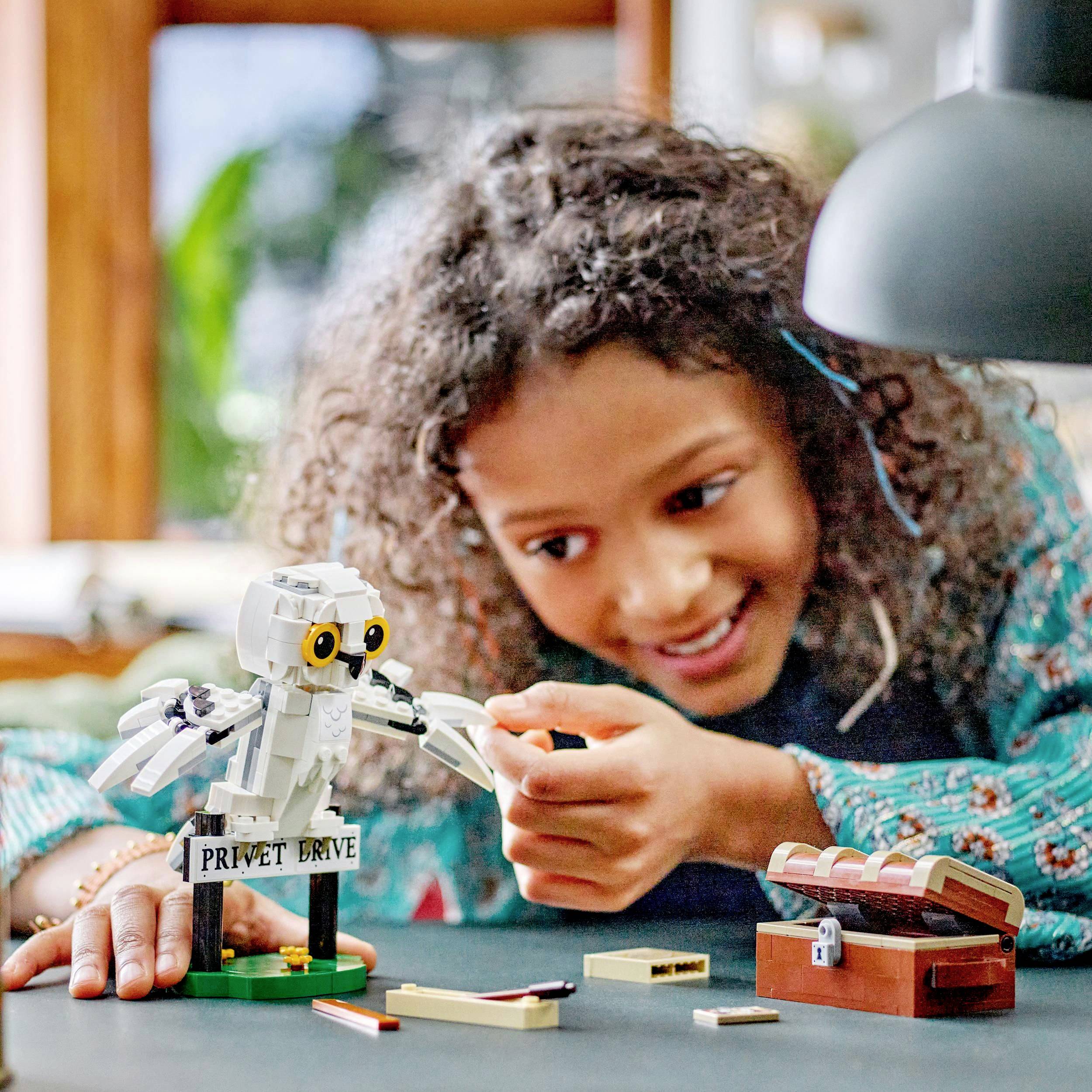Dijete se smiješi dok se igra Lego setom na stolu. Set prikazuje scenu s figurom i natpisom 'Privet Drive'.