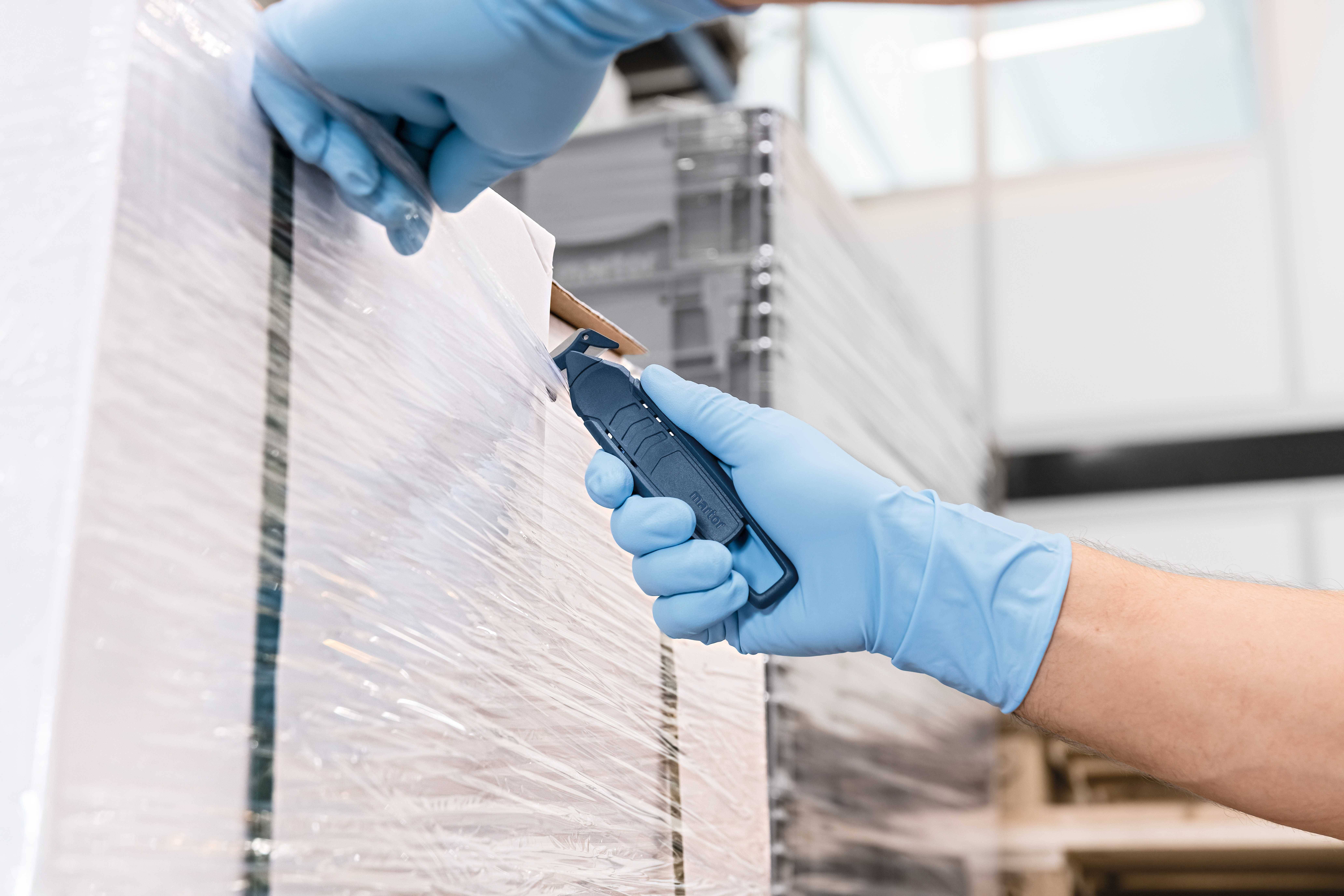 Osoba u plavim rukavicama nožem reže plastičnu foliju s palete.