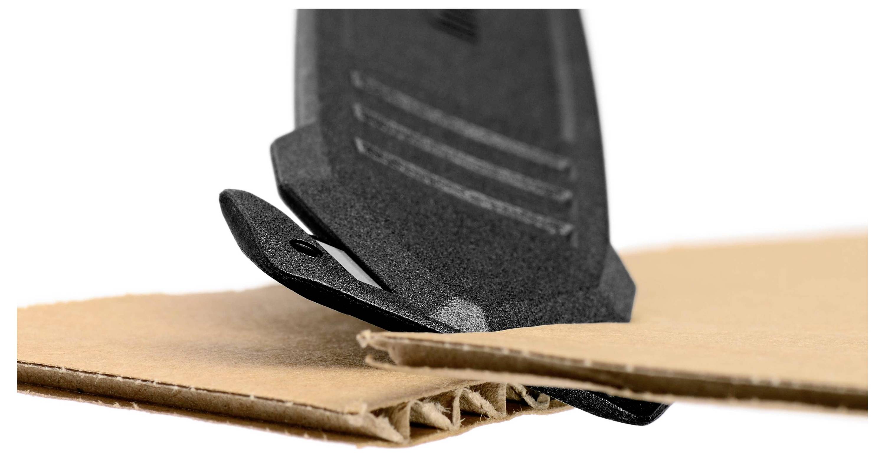 Crna rezačka alat reže kroz valoviti karton. Alat ima oštricu i postavljen je nagnut u odnosu na karton.