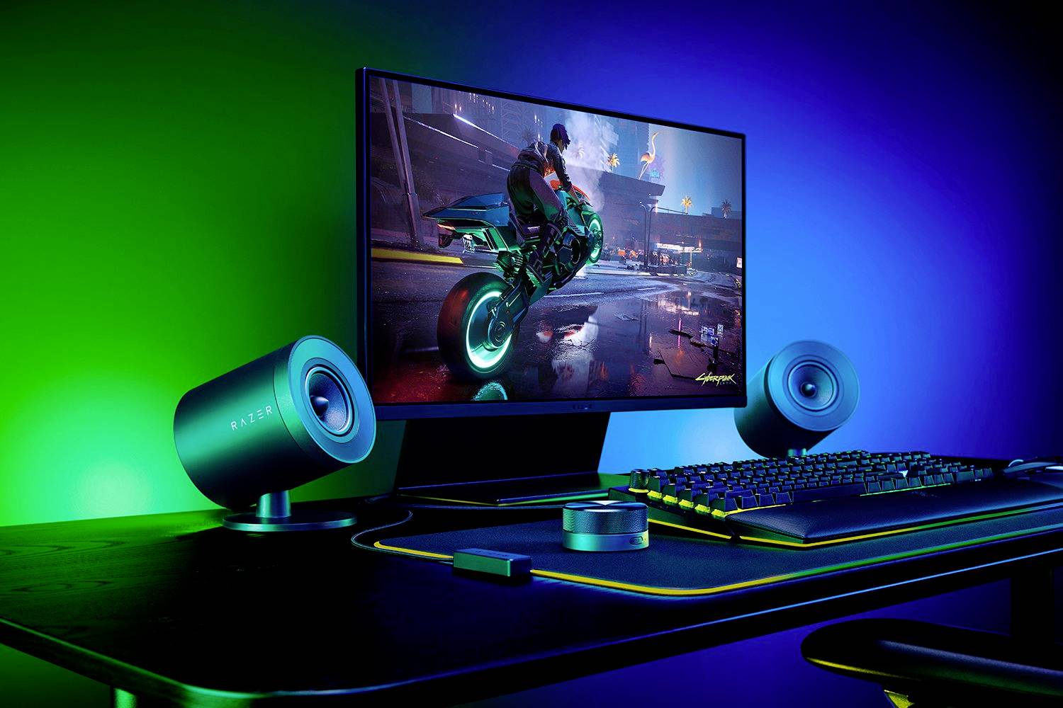 Računalni ekran prikazuje futurističku igru s motorciklom. Gaming postav s tipkovnicom i zvučnicima je vidljiv.