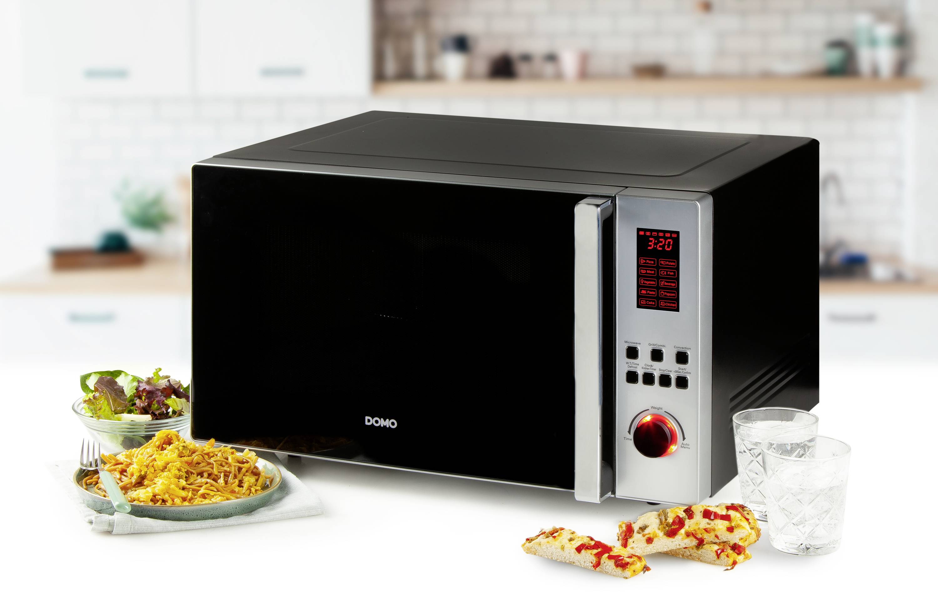 Crna mikrovalna pećnica na kuhinjskoj radnoj ploči, pokraj tanjura s jjelom od tjestenine, kriškama pizze i dva čaša vode.