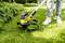 Osoba kosi travnjak žutim trimmerom preko zelene trave. Osoba nosi traperice i bijele tenisice.