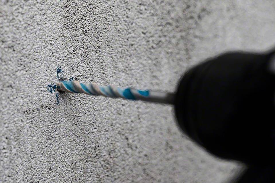 Osoba bušilica električno buši rupu u betonskom zidu, s fokusom na svrdlo i površinu zida.