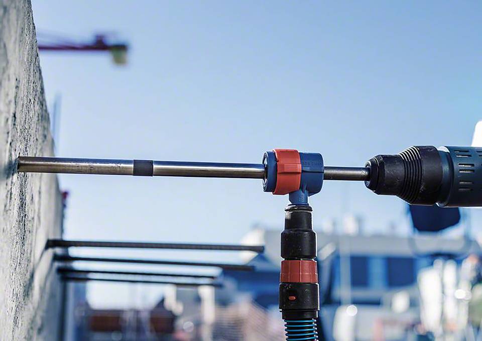 Bušilica buši rupu u betonski zid na otvorenom prostoru. U pozadini se nejasno naziru strukture zgrada.