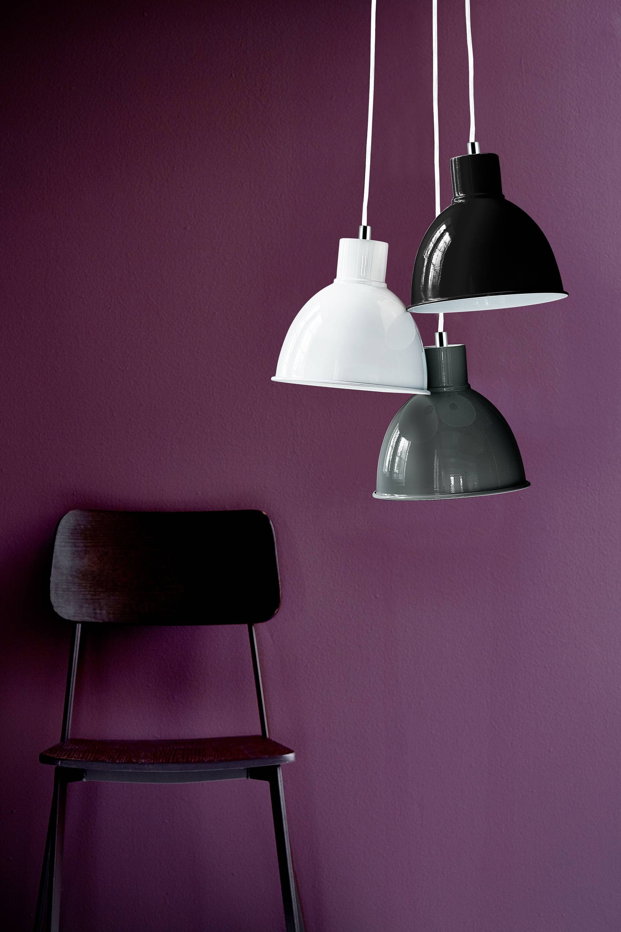 Tri viseće lampe u bojama bijela, crna i siva ispred ljubičaste stjenke iznad drvenog stolca.