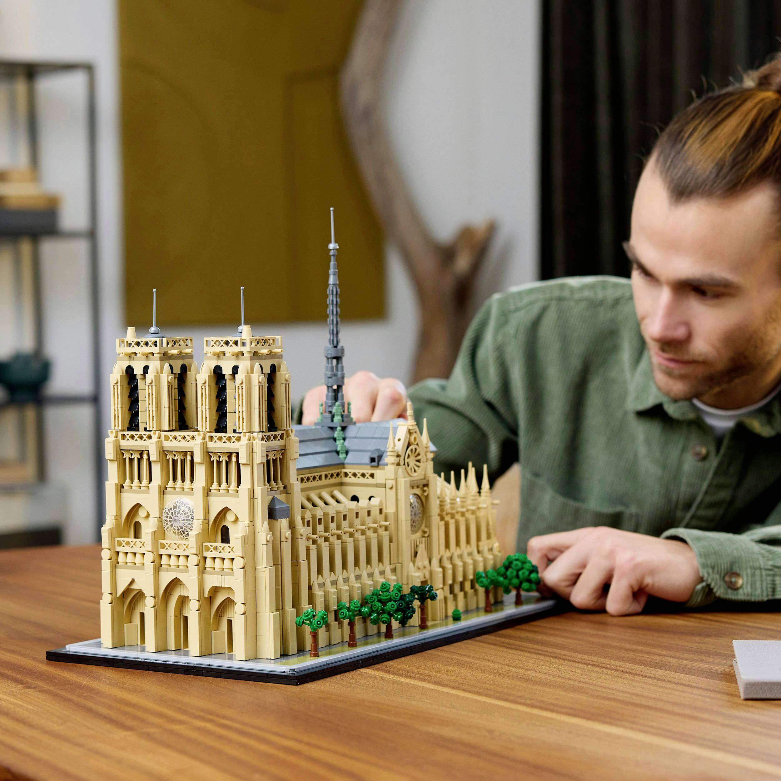 Čovjek gradi detaljan model katedrale Notre-Dame pomoću malih građevinskih elemenata. U pozadini se naziru police.
