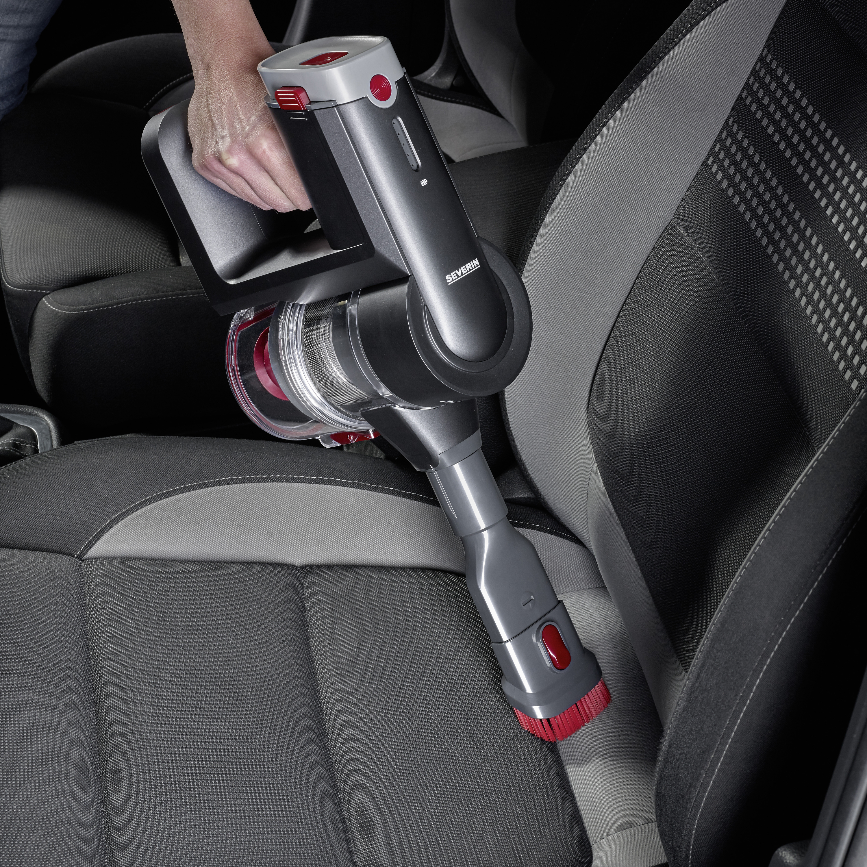 Jedna osoba usisava sjedalo automobila bežičnim ručnim usisivačem. Usisivač je mali i praktičan.
