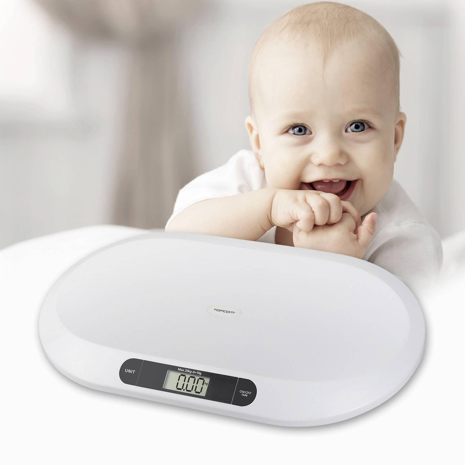 Nasmijeno dijete sjedi iza digitalne vage za bebe koja pokazuje težinu od '0,00 kg'.