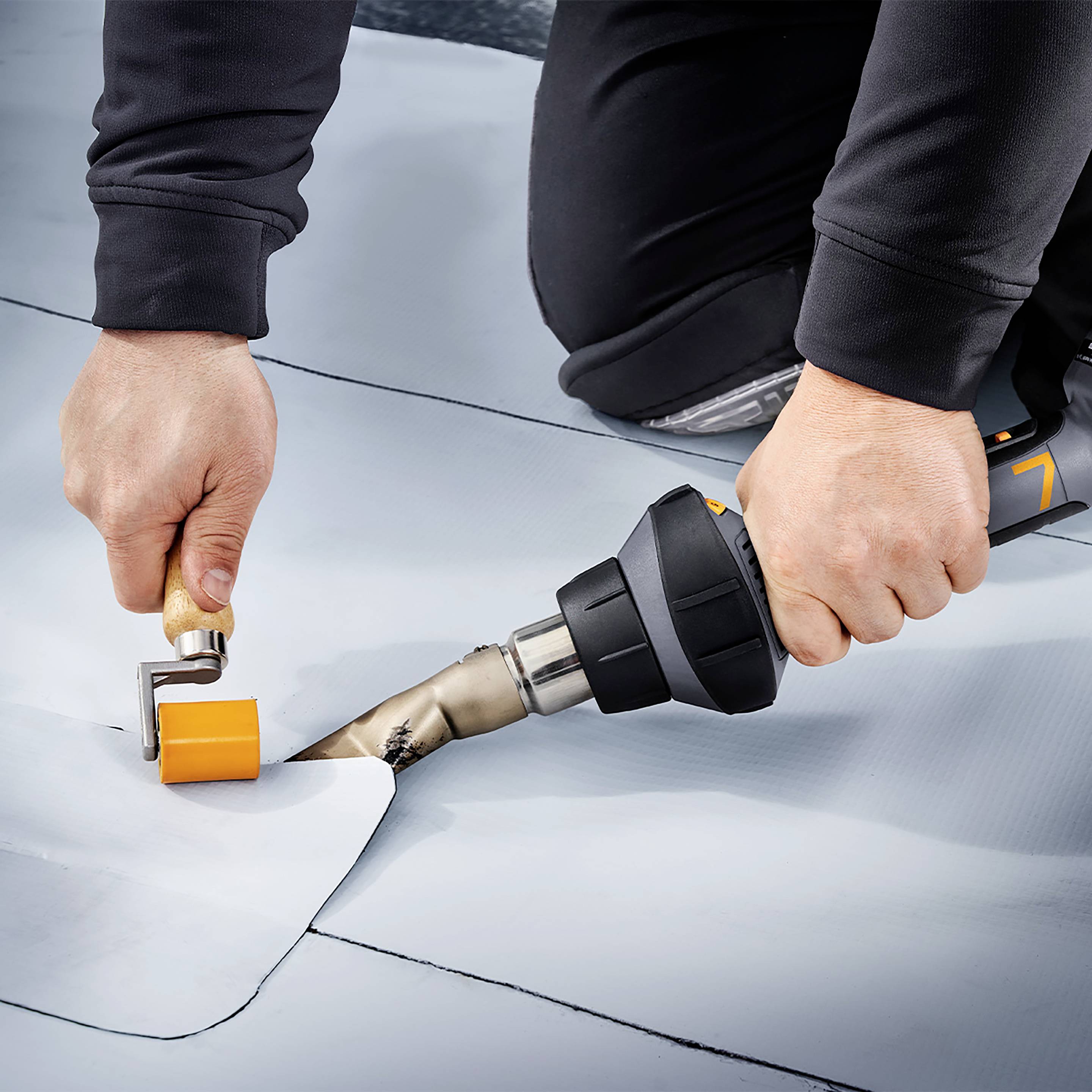 Jedna osoba zavaruje sivi plastični sloj pomoću specijalnog uređaja vrućeg zraka, istovremeno poravnavajući šav ručnim valjkom.