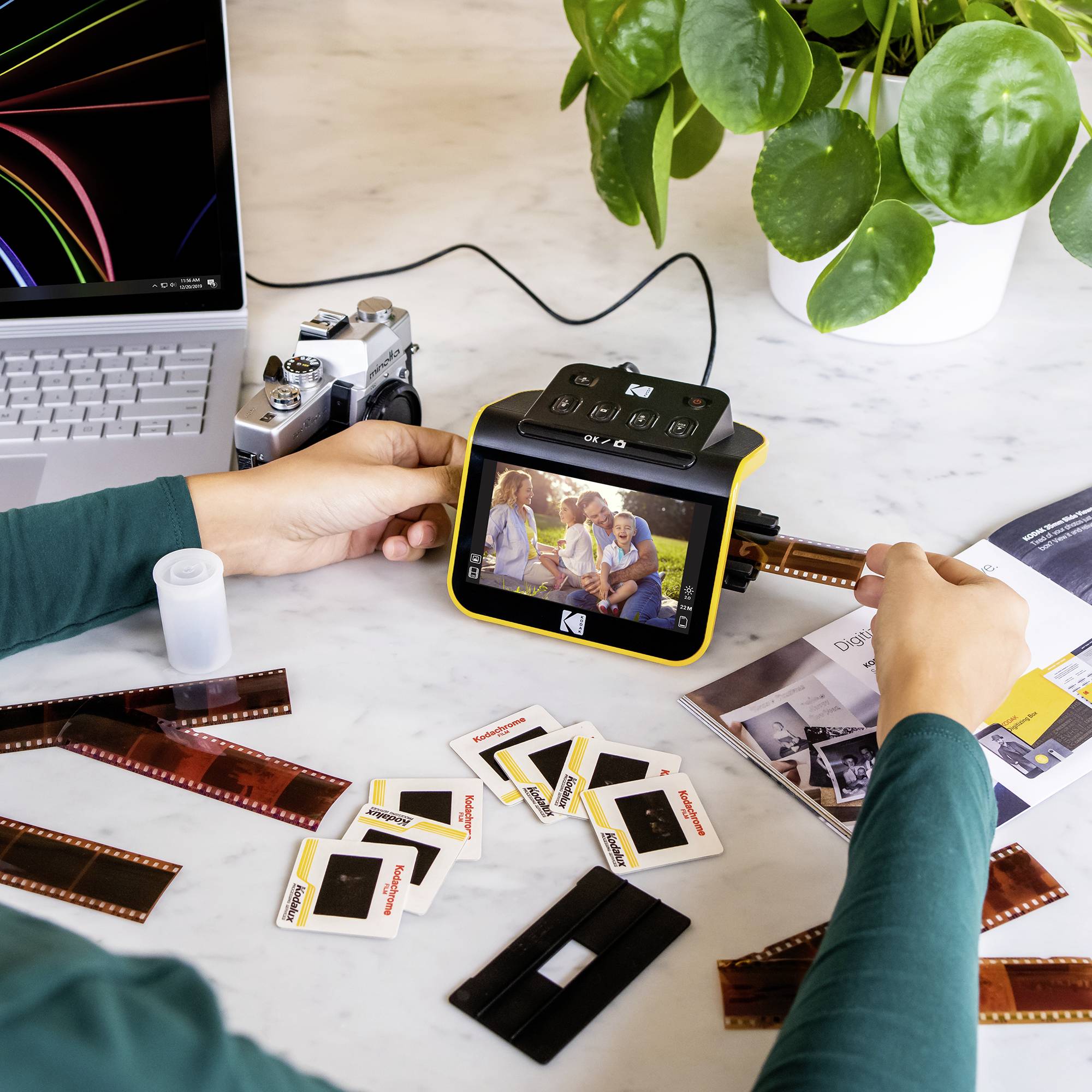 Jedna osoba digitalizira analogne foto-negative pomoću skenera. Na stolu leži laptop, filmske trake i fotoaparat.