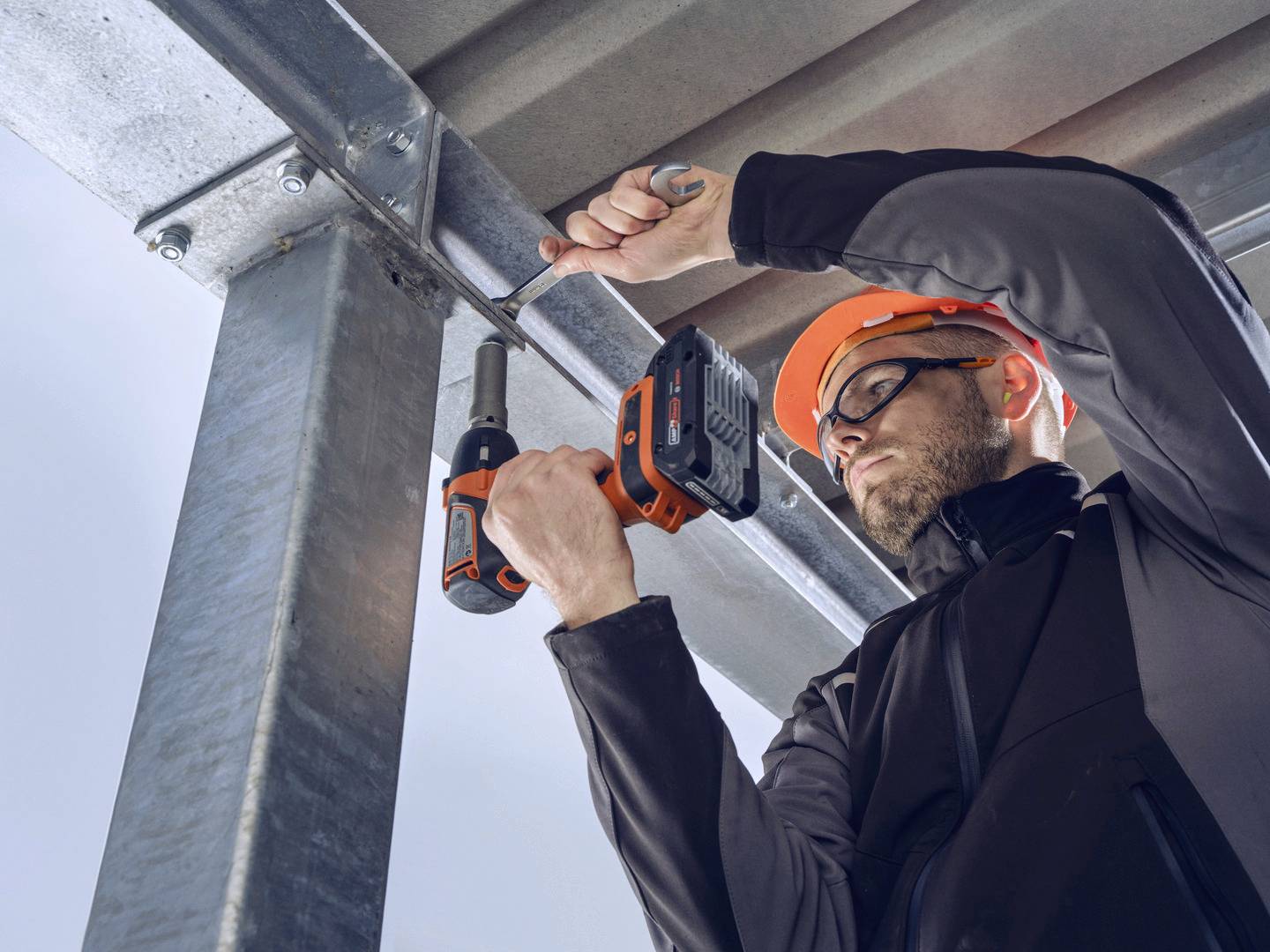 Radnik na gradilištu s zaštitnom kacigom koristi akumulatorski odvijač kako bi učvrstio metalne stepeničarske ograde.